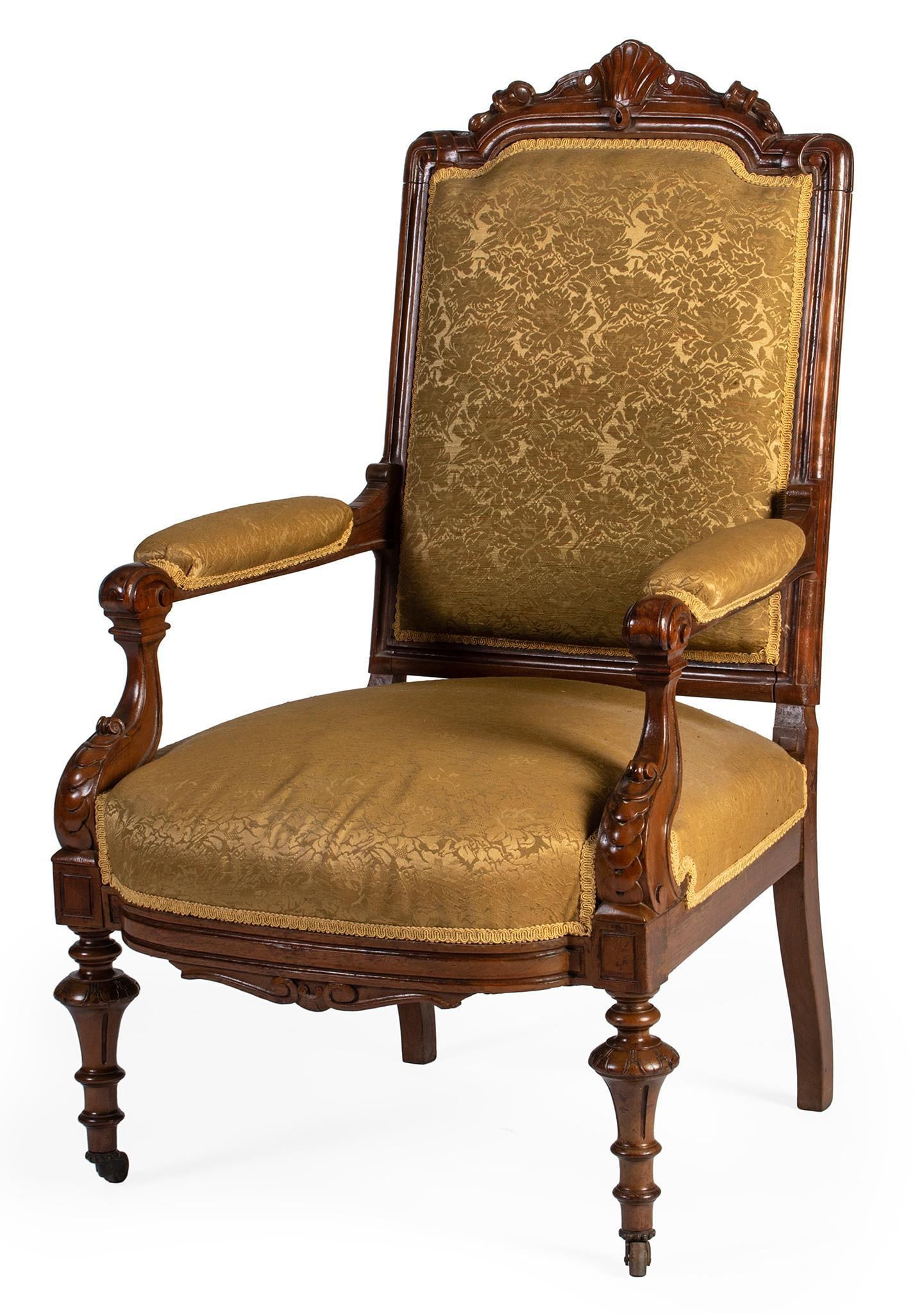 An Upholstered Victorian Eastlake Armchair: American, 19th century. An Eastlake armchair in walnut, having a central shell and scroll carved crest and fluted stiles, upholstered back and arms with shaped and carved supports, the upholstered sea