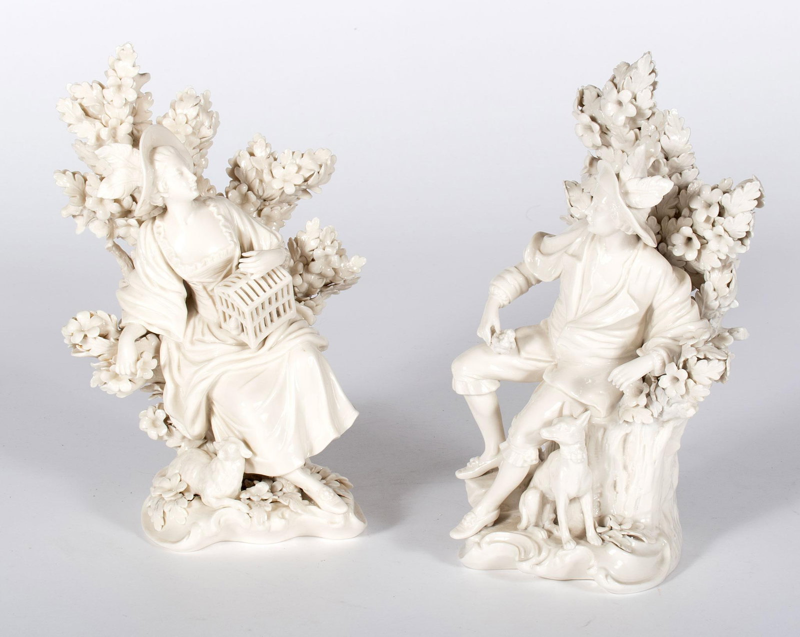 Continental Shepherd and Shepherdess Porcelain Figures: Continental, late 19th or early 20th century. Pair of porcelain shepherd and shepherdess figures, each sitting on tree stump, male with bird and dog & female with cage and sheep, each with cobalt 