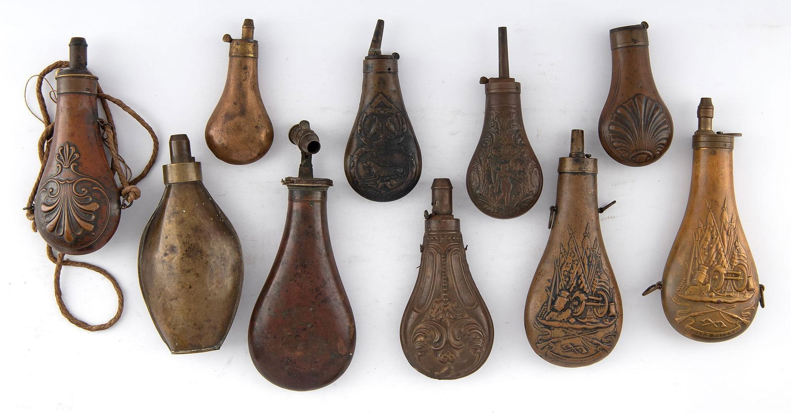 Lot Of Ten Shell and Scene Designed Powder Flasks: Comprising ten (10) shell-embossed and scene-decorated powder flasks, each fitted with spouts, several retaining hanging rings. Largest flask measures 8 inches in length. Some complete, others missing