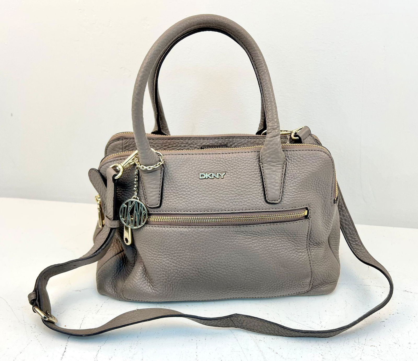 A DKNY Brown Leather Handbag with Shoulder Strap. Gold-tone hardware. Exterior zipped compartment.: A DKNY Brown Leather Handbag with Shoulder Strap. Gold-tone hardware. Exterior zipped compartment. Three inner compartments ( two are zipped). Monogram cloth interior. Please see photos for conditions