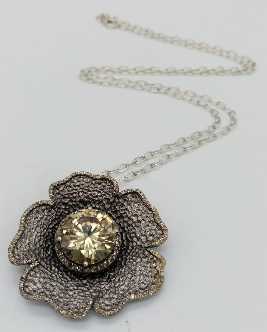 A Champagne Moissanite Flower Brooch/Pendant in an Antique Design on a 925 Silver Chain. Moissanite: A Champagne Moissanite Flower Brooch/Pendant in an Antique Design on a 925 Silver Chain. Moissanite weight 15 ct and diamonds 1.85ct. 4cm and 58cm. Comes with a presentation case.