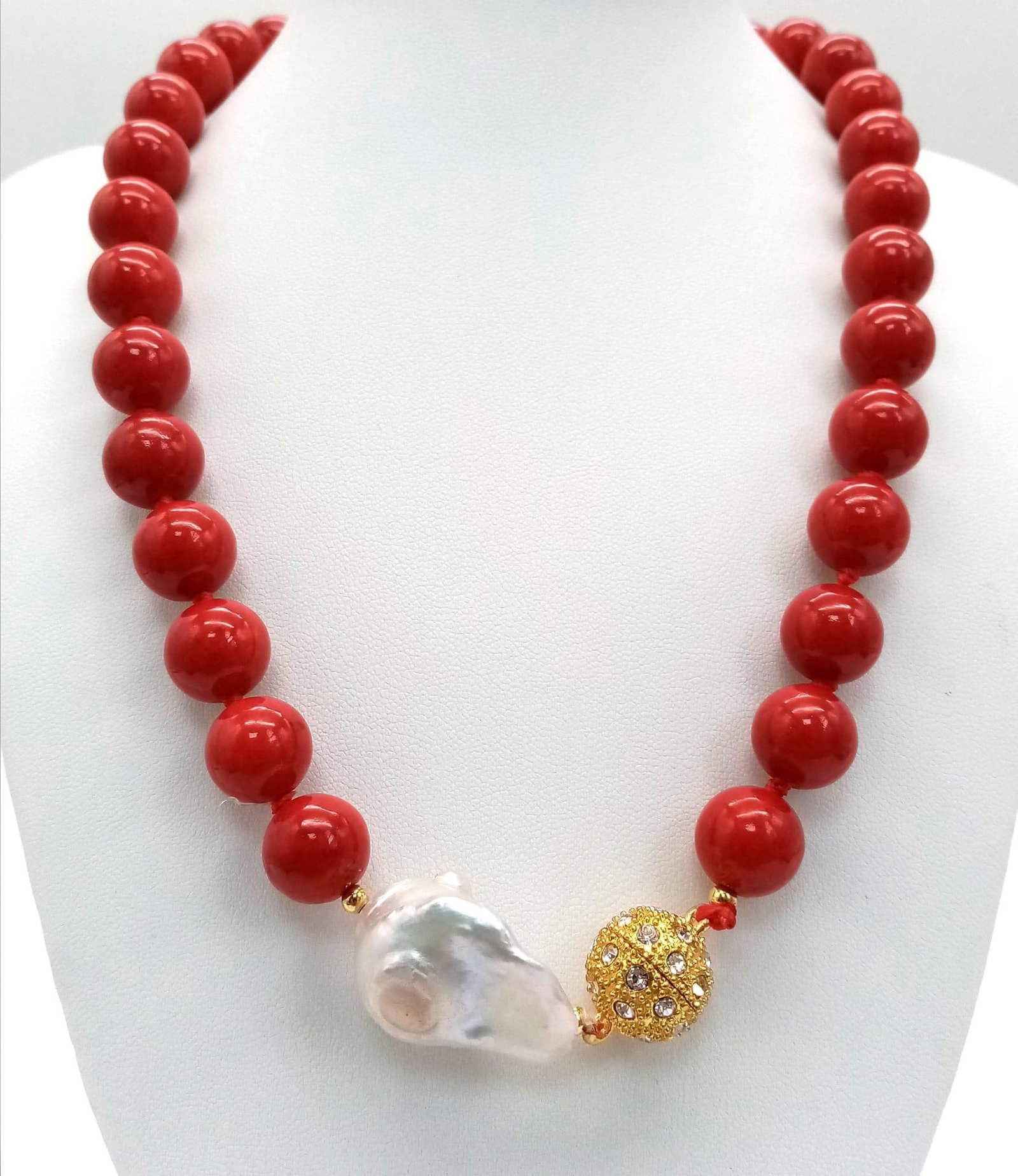 A Red Coral And Baroque Pearl Necklace. 12mm beads with a large irregular shaped baroque pearl: A Red Coral And Baroque Pearl Necklace. 12mm beads with a large irregular shaped baroque pearl interrupter. Glitter ball clasp. 44cm necklace length.