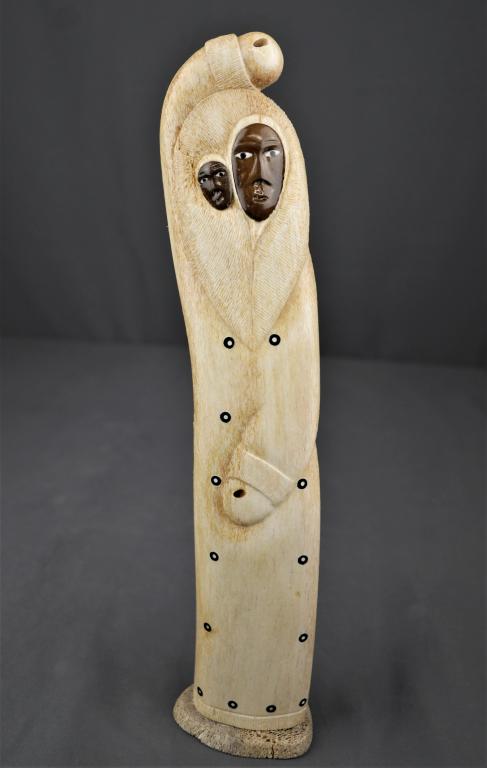 Ray Weyiouanna Inuit Whale Bone Carved Sculpture: Ray Weyiouanna (Inupiat, Alaska). Hand Carved Whale Bone Sculpture depicting an Inuit woman holding her child. Has "Authentic Native Handicraft from Alaska" sticker on back. Signed by artist lower bac