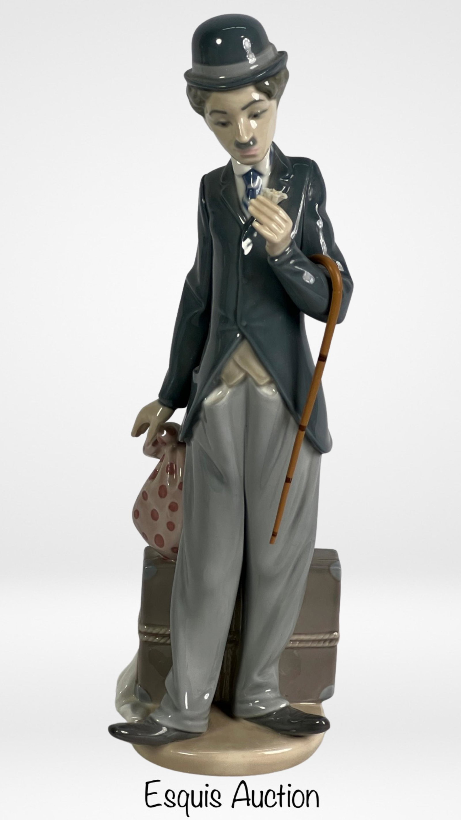 Lladro- Charlie the Tramp 5233 Porcelain Figurine: The Lladro Figurine 5233 "Charlie The Tramp" is a charming porcelain representation of the iconic comedian Charlie Chaplin. Standing at 11 1/4" tall, this figurine captures the essence of the beloved 