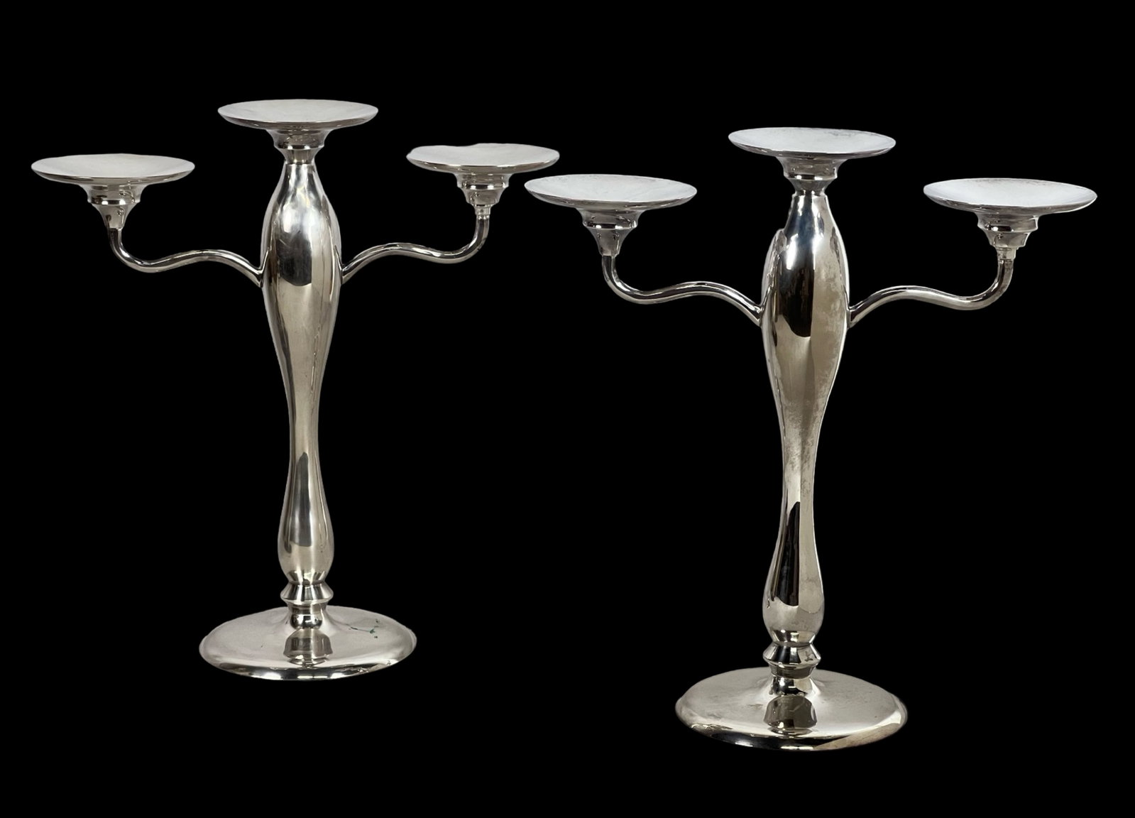 Pair of Elegant Silverplate Candelabras: A sophisticated pair of silver-plated candelabras, each standing 15" tall and measuring 14" wide. These stylish pieces feature graceful curves and a sleek, timeless design, perfect for enhancing any e