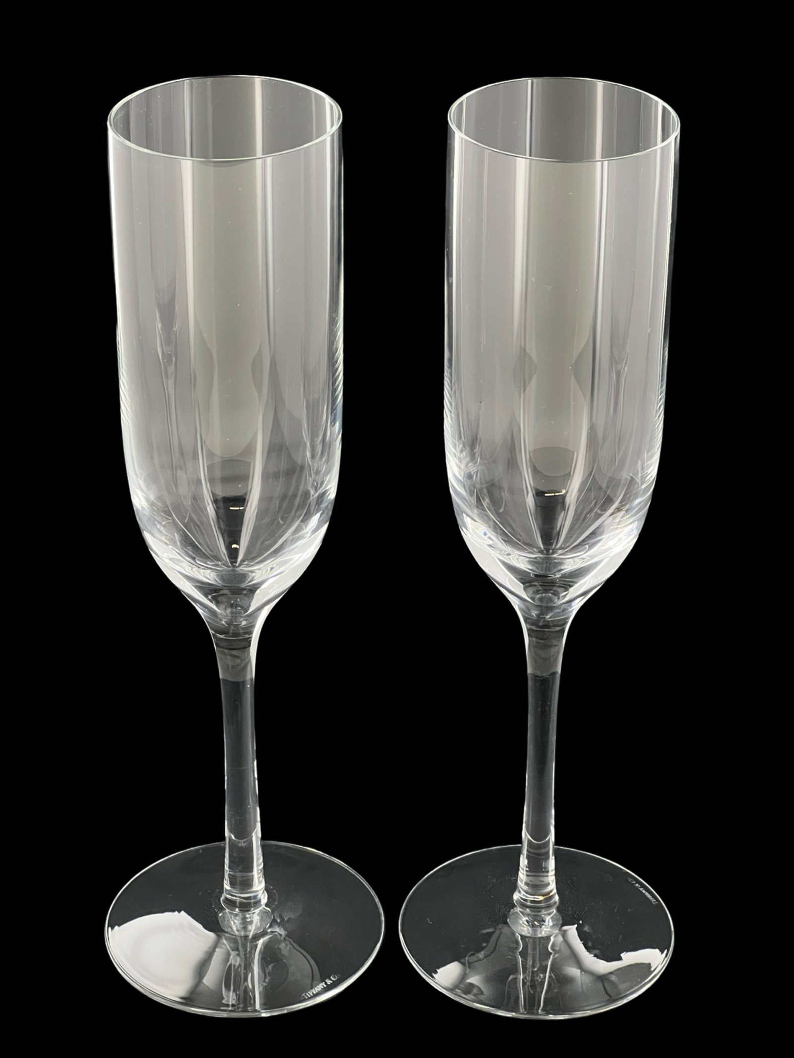 Tiffany & Co. Crystal Champagne Flutes: This elegant set of two Tiffany & Co. crystal champagne flutes stands 9" tall and features sleek vertical etching patterns. Both glasses are etched with the "Tiffany & Co." mark on the base, represent