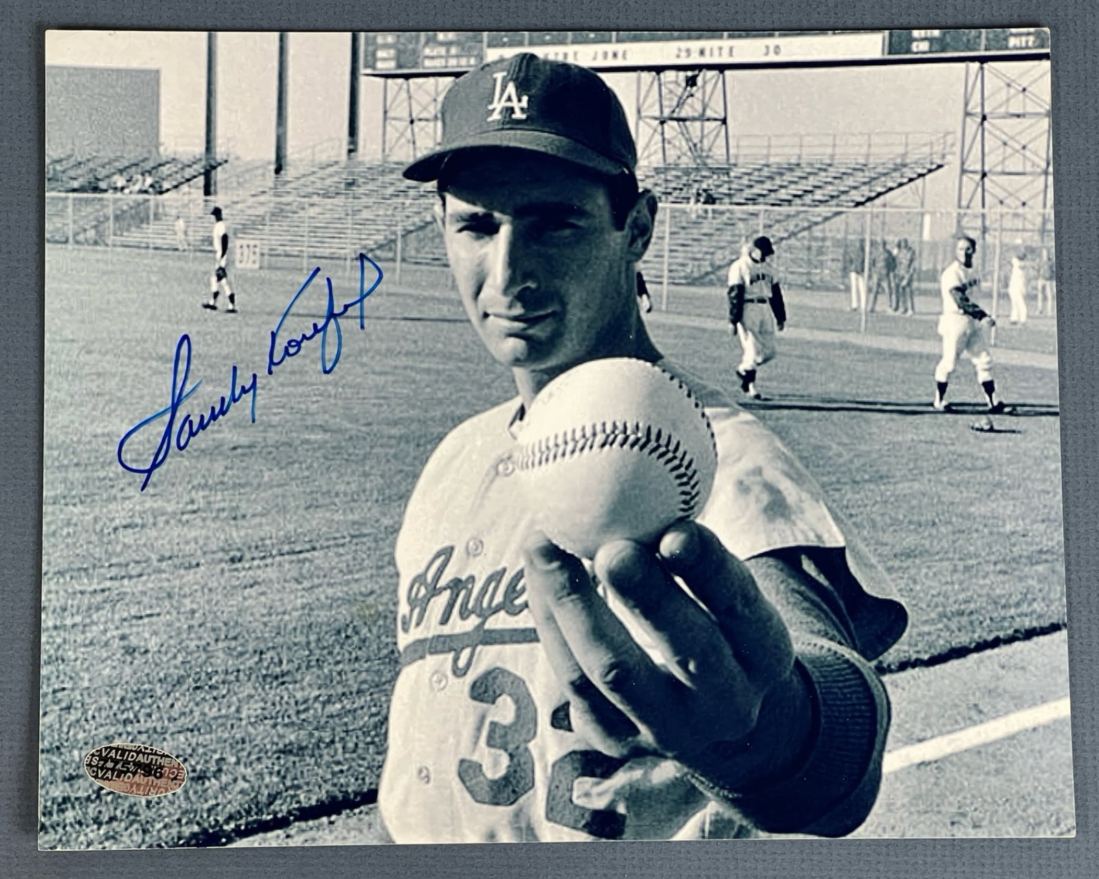 Sandy Koufax Autographed Photograph: A signed black-and-white photograph of legendary pitcher Sandy Koufax in his Los Angeles Dodgers uniform. The iconic image features Koufax holding a baseball up close to the camera, with his signature