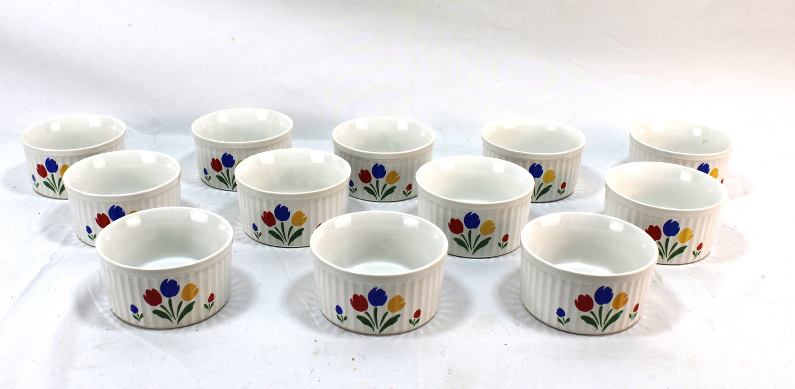 Set of 12 Vintage Ceramic Ramekins with Floral Tulip Design: Charming set of 12 vintage ceramic ramekins featuring colorful tulip floral designs. Each ramekin showcases a ribbed exterior with vibrant red, blue, and yellow tulip accents, adding a cheerful, retro