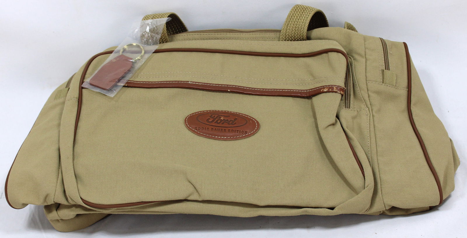 Ford Eddie Bauer Edition Duffel Bag with Original Keychain Collectible: Ford Eddie Bauer Edition duffel bag crafted from durable beige canvas with leather trim and accents, featuring the iconic Eddie Bauer branding. Includes an original leather keychain still in its packa