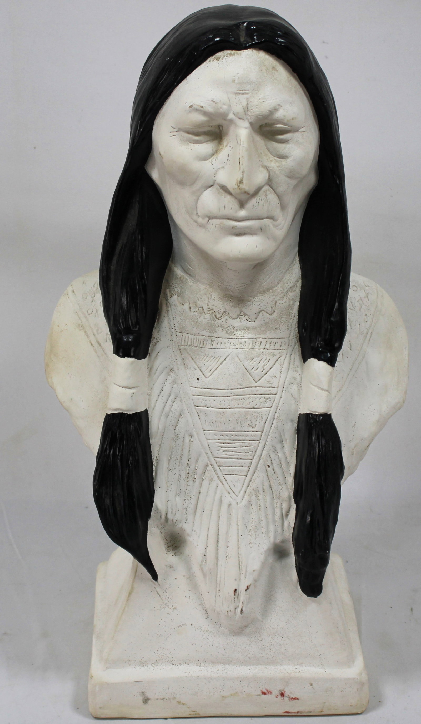 Vintage Native American Bust with Braided Hair and Tribal Details: Striking bust sculpture of a Native American elder, crafted with detailed features and traditional attire. The black braided hair and intricate carvings on the clothing highlight the craftsmanship. A 