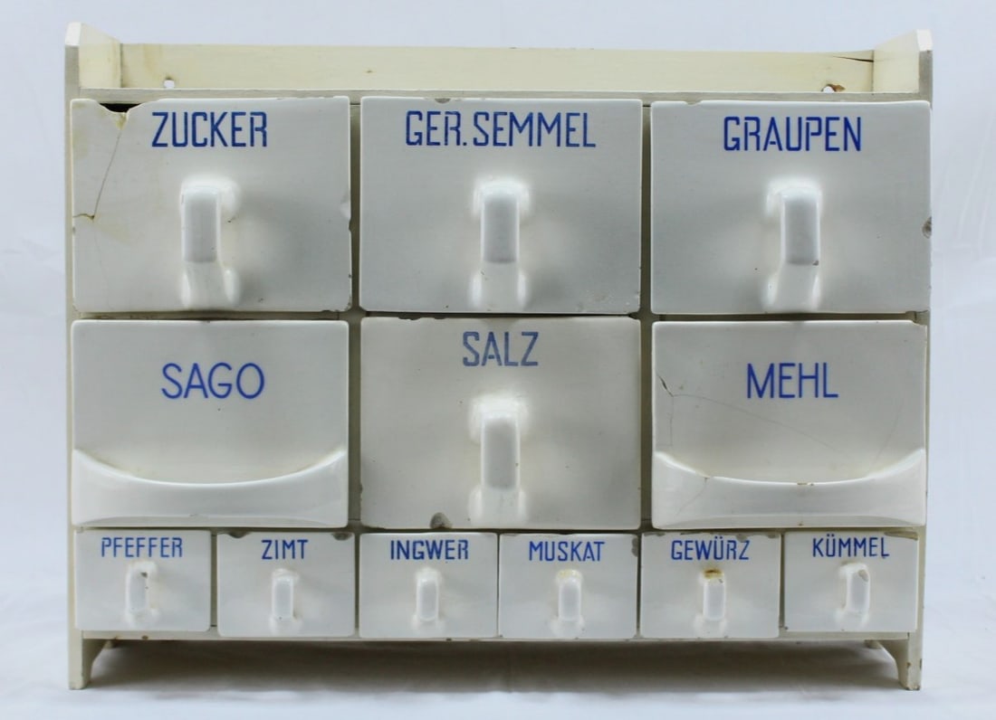 Antique German Porcelain Spice Cabinet: Antique German porcelain spice cabinet featuring labeled drawers for ingredients.The cabinet includes a charming wooden frame and porcelain knobs. Drawers show cracks and wear, consistent with age and
