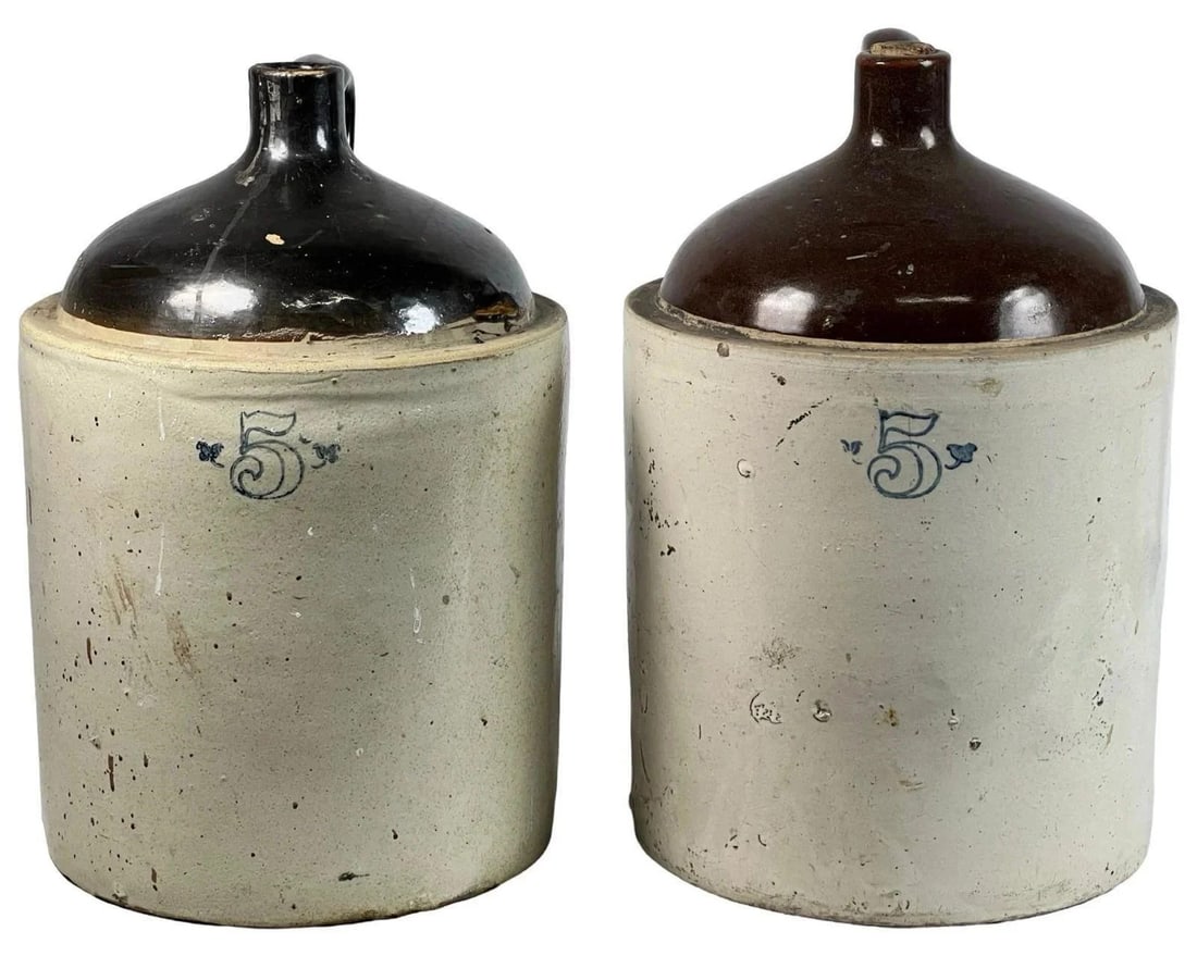 Two Antique 5-Gallon Stoneware Whiskey/Wine Jugs: Pair of Antique 5-gallon stoneware whiskey or wine jugs featuring classic cream-colored bases with dark brown glazed tops. Each jug is adorned with a single side handle for easy carrying. A timeless p