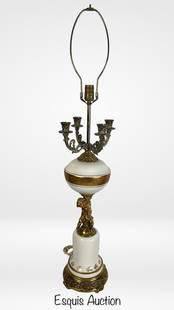 Hollywood Regency Lamp w/ Cherub & Candelabra Arms: This dramatic Hollywood Regency table lamp stands an impressive 42 inches tall and features an ornate composition blending white porcelain with elaborate gilt brass detailing. At its center is a finel