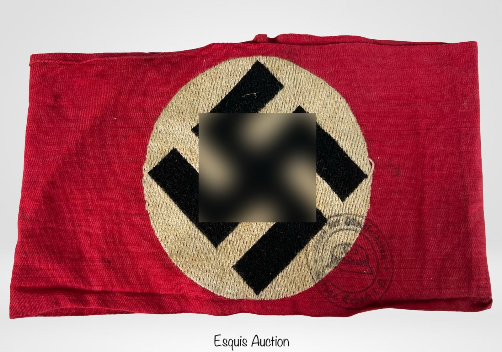 WWII German Armband with Period Stamp: WWII German red armband featuring a white roundel with black woven emblem. The piece bears an official ink stamp along the edge, partially legible, with Gothic script and a helmet motif, indicative of