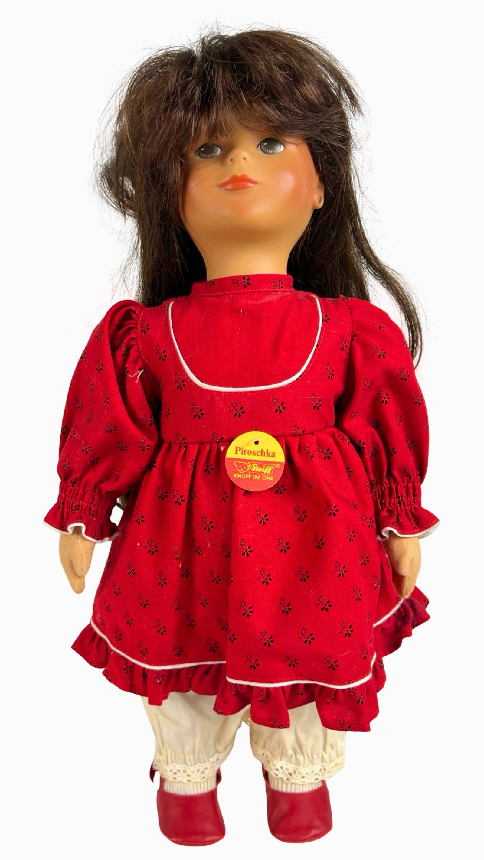 Steiff "Piroschka" Doll with Red Dress: Charming Steiff "Piroschka" doll, measuring 17" tall, dressed in a vibrant red patterned dress with matching apron, white lace-trimmed pantaloons, and red shoes. She has long brunette hair tied with a