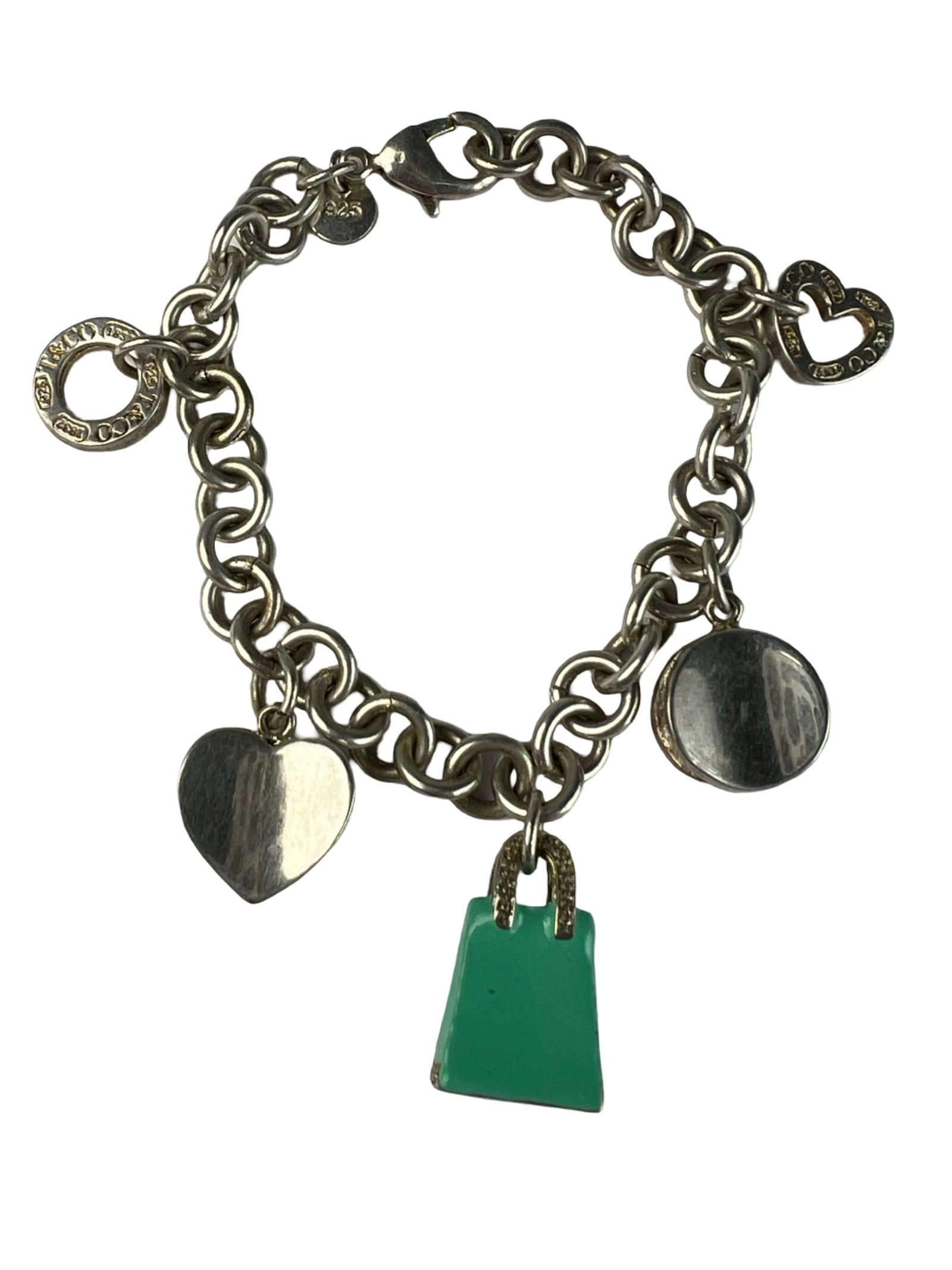 Charm Bracelet with Mixed Charms: Stylish charm bracelet featuring an assortment of playful and elegant charms, including a heart, open circle, round tag, and a green enamel shopping bag. The bracelet measures approximately 7 1/2" lon