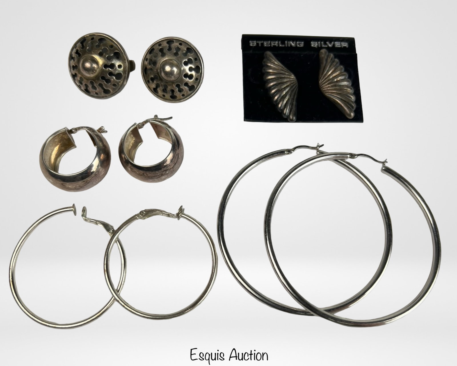 Group of Massive Sterling Silver Earrings: Selection of bold sterling silver earrings featuring diverse statement designs. Includes circular domed studs with openwork detailing, sculptural wing-form earrings, chunky hoops, and oversized minima