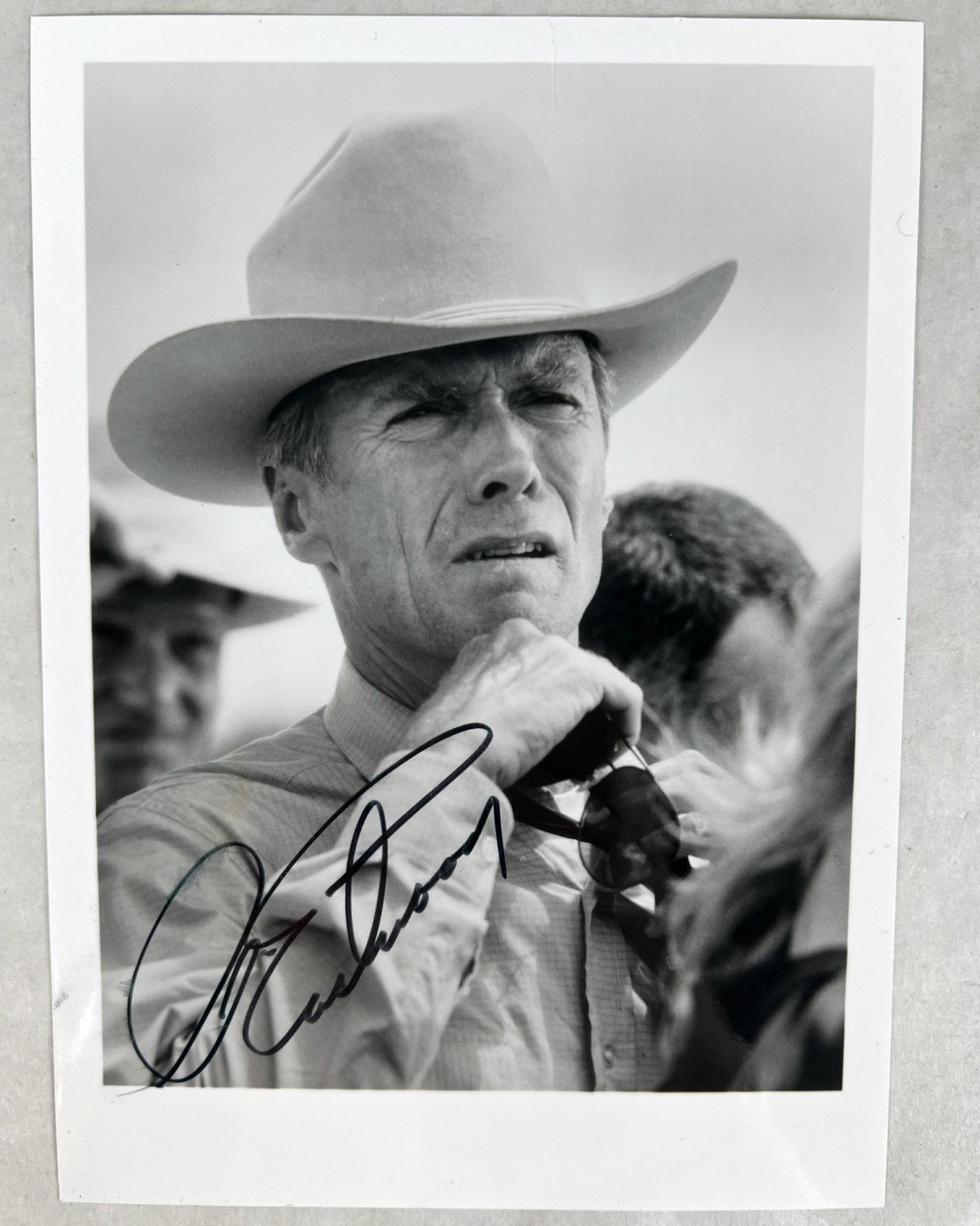Clint Eastwood - Signed Black & White Cowboy Photo: Classic black-and-white portrait of Clint Eastwood, captured in a defining Western pose with hat and neckerchief. Boldly autographed in black ink, this evocative image reflects Eastwood's enduring pre
