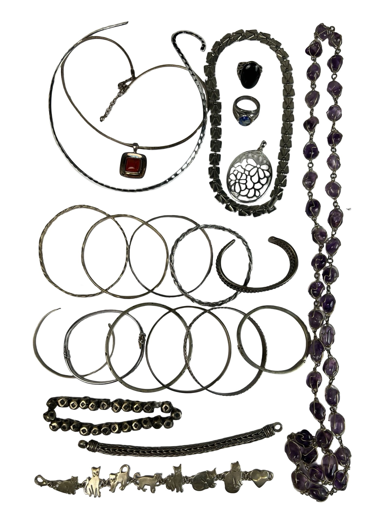 Silver-Tone Jewelry Collection: Diverse assortment of silver-tone jewelry including bangles, cuffs, necklaces, pendants, and rings. The group features a variety of styles such as a red stone pendant necklace, cat motif bracelet, ame
