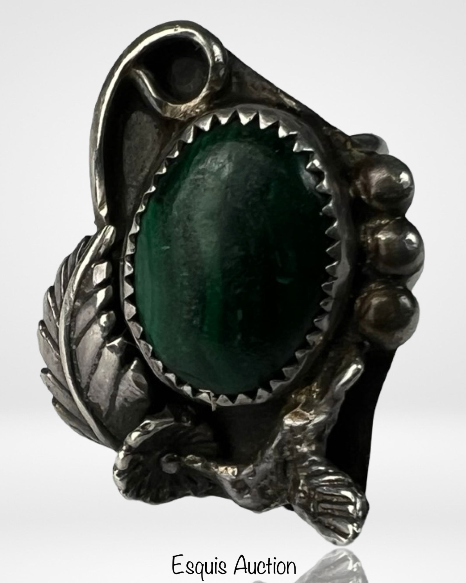 Native American Sterling Silver & Malachite Ring: Striking Native American ring featuring a rich green malachite cabochon set in a serrated bezel. The stone is framed with traditional sterling silver accents including a feather motif, curling vine de