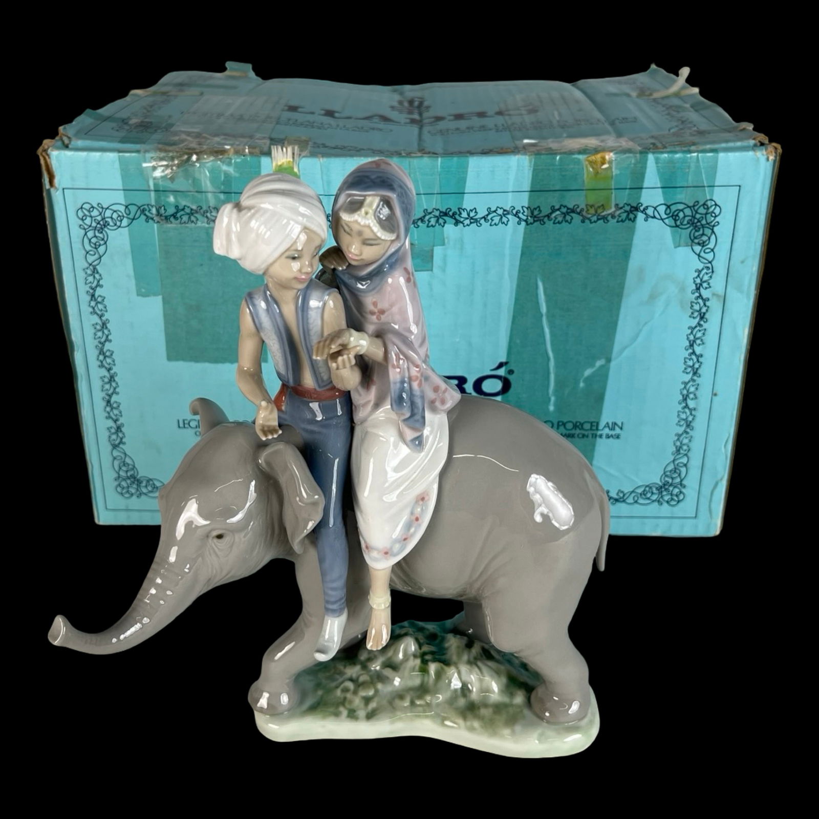 Lladro Hindu Children on Elephant Figurine: Charming Lladro hand-painted porcelain sculpture titled Hindu Children on Elephant, model #5352. This delightful piece depicts a young boy and girl in traditional attire seated atop a gentle elephant,