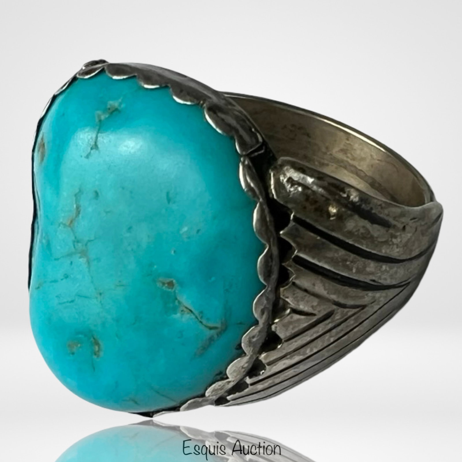 Native American Sterling Silver Turquoise Ring: Bold Native American sterling silver ring showcasing a substantial freeform turquoise stone with natural matrix, framed by a finely scalloped bezel. The thick band features deep chiseled lines radiati
