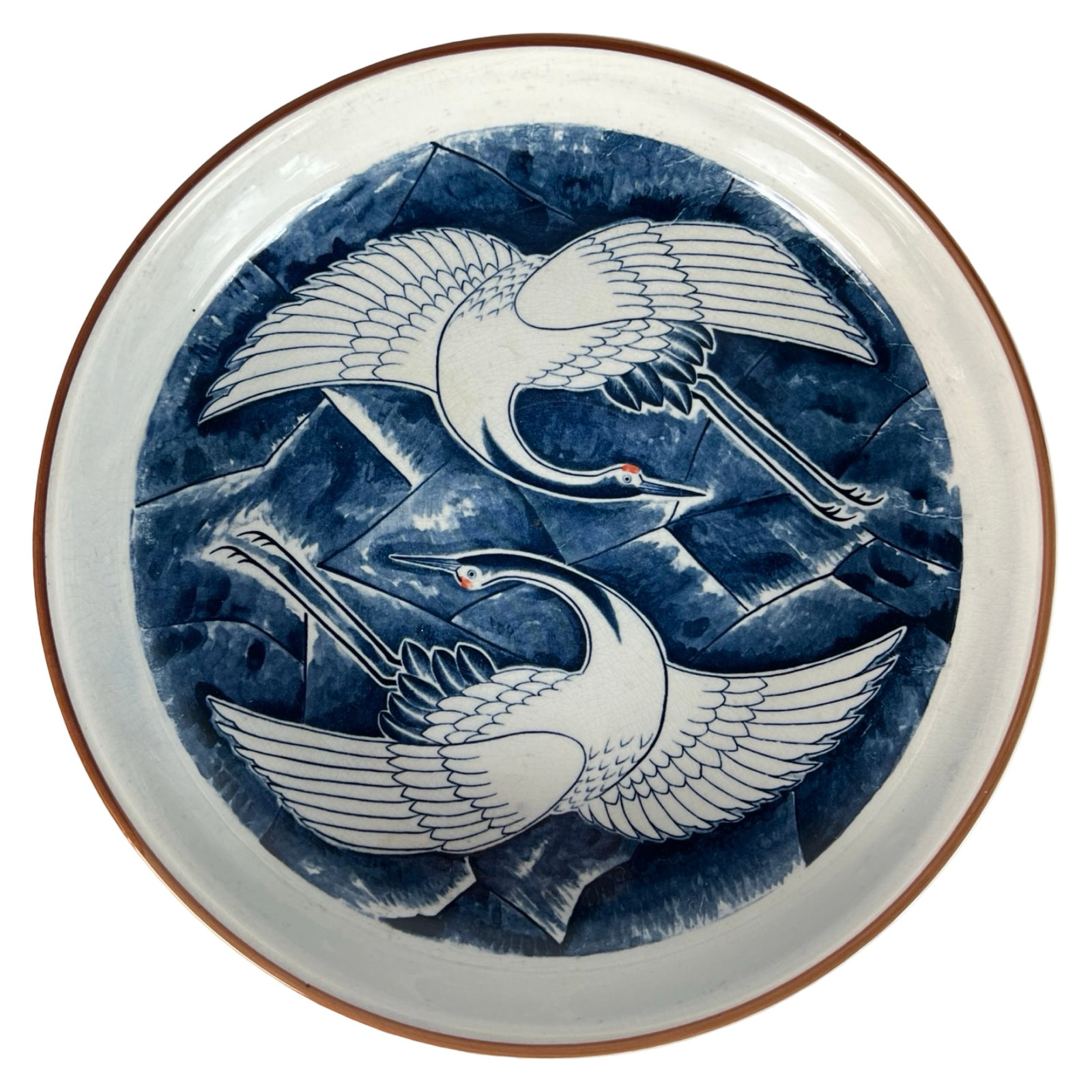 Japanese Porcelain Charger with Flying Cranes: Decorative Japanese porcelain charger featuring a dynamic scene of two stylized white cranes in flight, set against a rich indigo blue abstract background. The rim is subtly accented with a reddish-br