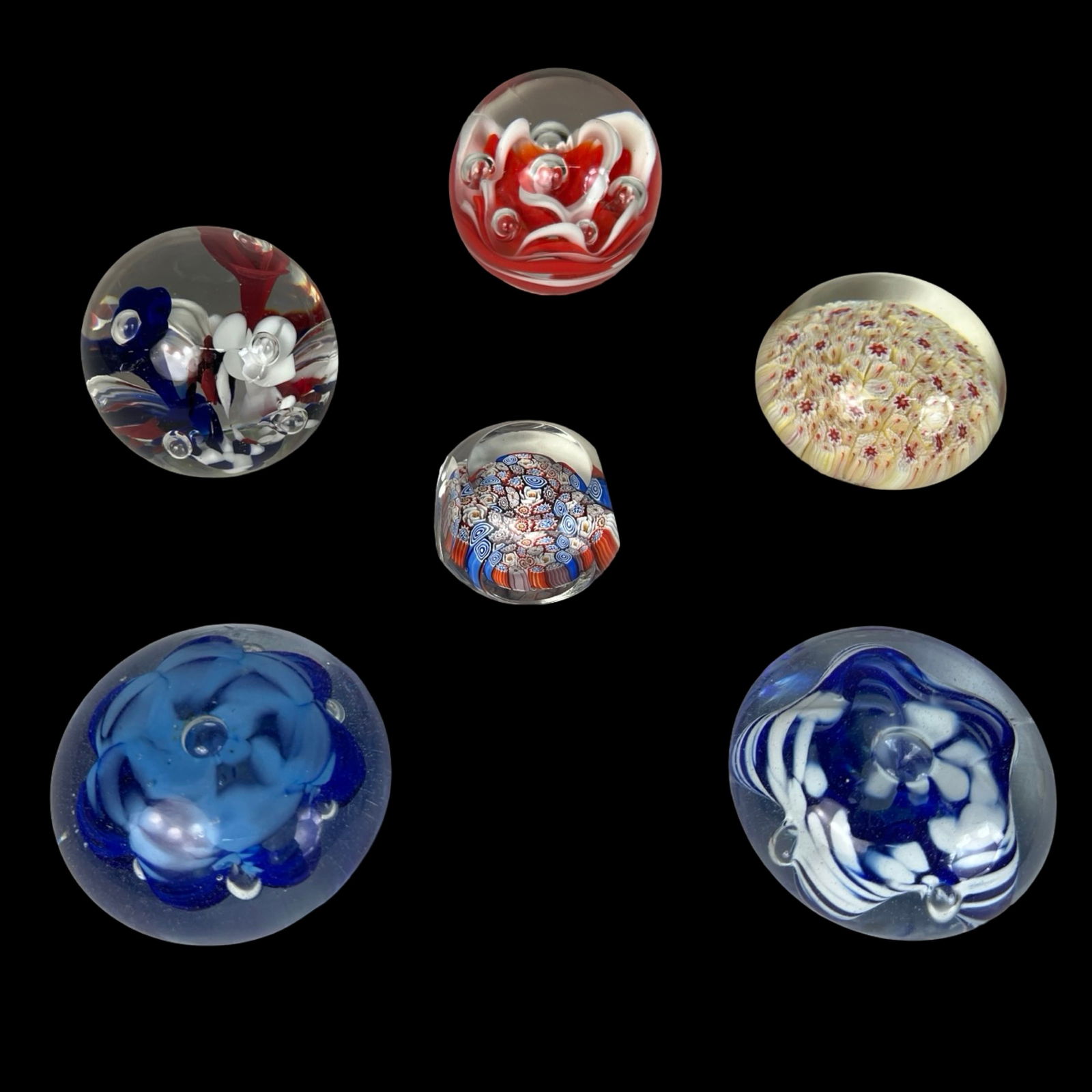 Collection of Art Glass Paperweights: Colorful assortment of six art glass paperweights, each showcasing unique techniques and vibrant internal designs. The group includes floral-style encased weights, millefiori elements, swirling abstra
