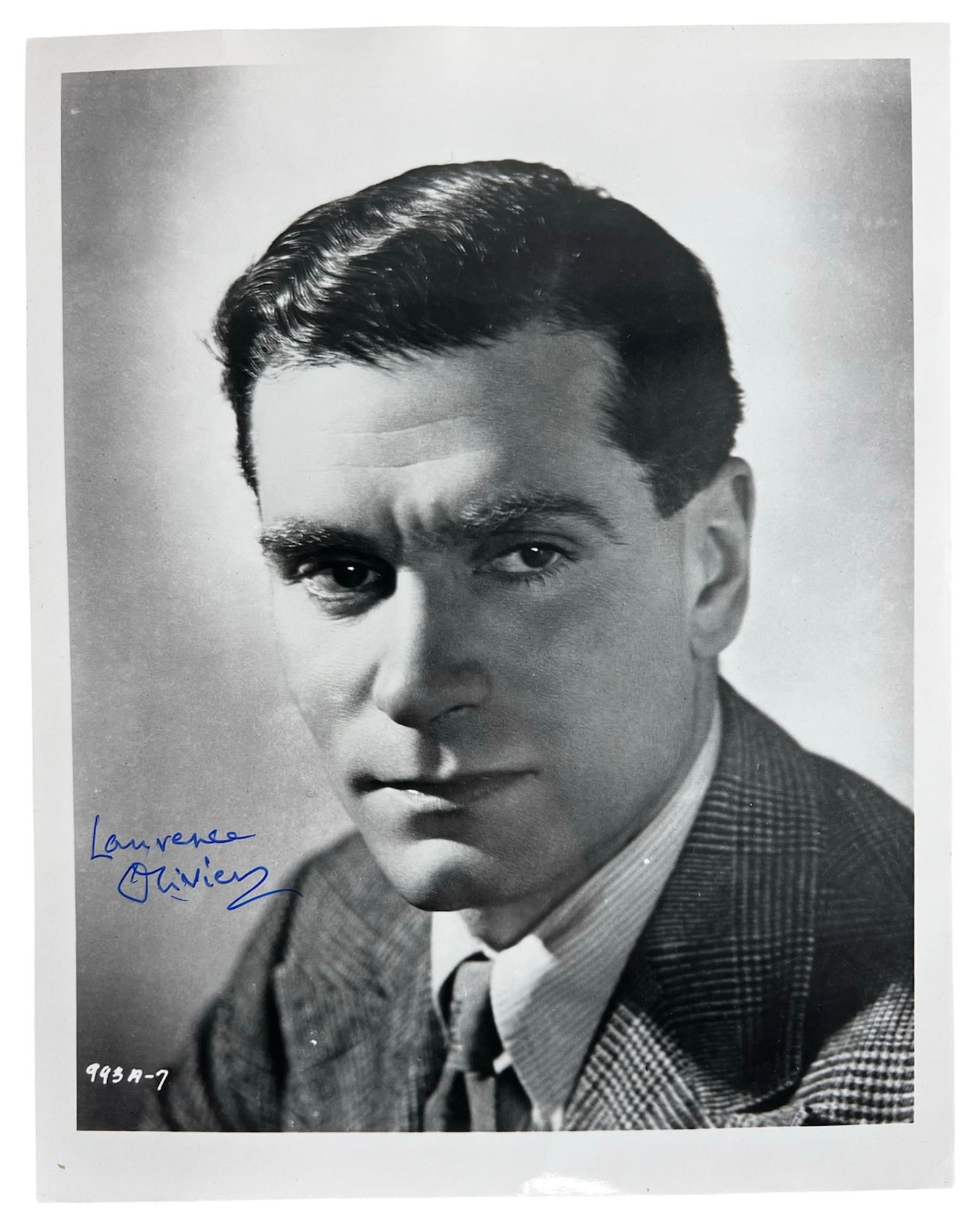 Laurence Olivier Autographed/ Signed Photograph: Striking vintage studio portrait of legendary British actor Laurence Olivier, signed in bold blue ink. Captured in a sharply dressed suit with a confident, brooding gaze, this black-and-white headshot