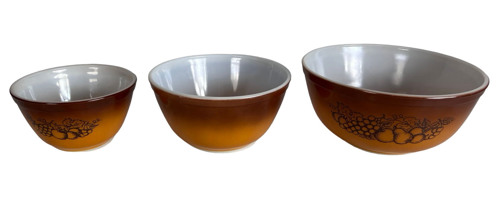 Vintage Pyrex "Autumn Harvest" Mixing Bowls: This vintage Pyrex mixing bowl set features the iconic "Autumn Harvest" pattern with a warm amber-to-brown gradient and black fruit and vegetable illustration around the exterior. The set includes thr