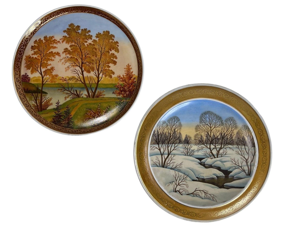 Russian Hand-Painted Porcelain Wall Chargers: Pair of hand-painted porcelain wall chargers by artist Alevtina Andreevna Gorkova, each depicting a beautifully rendered seasonal landscape. One plate, titled "Autumn," features a golden-hued riversid