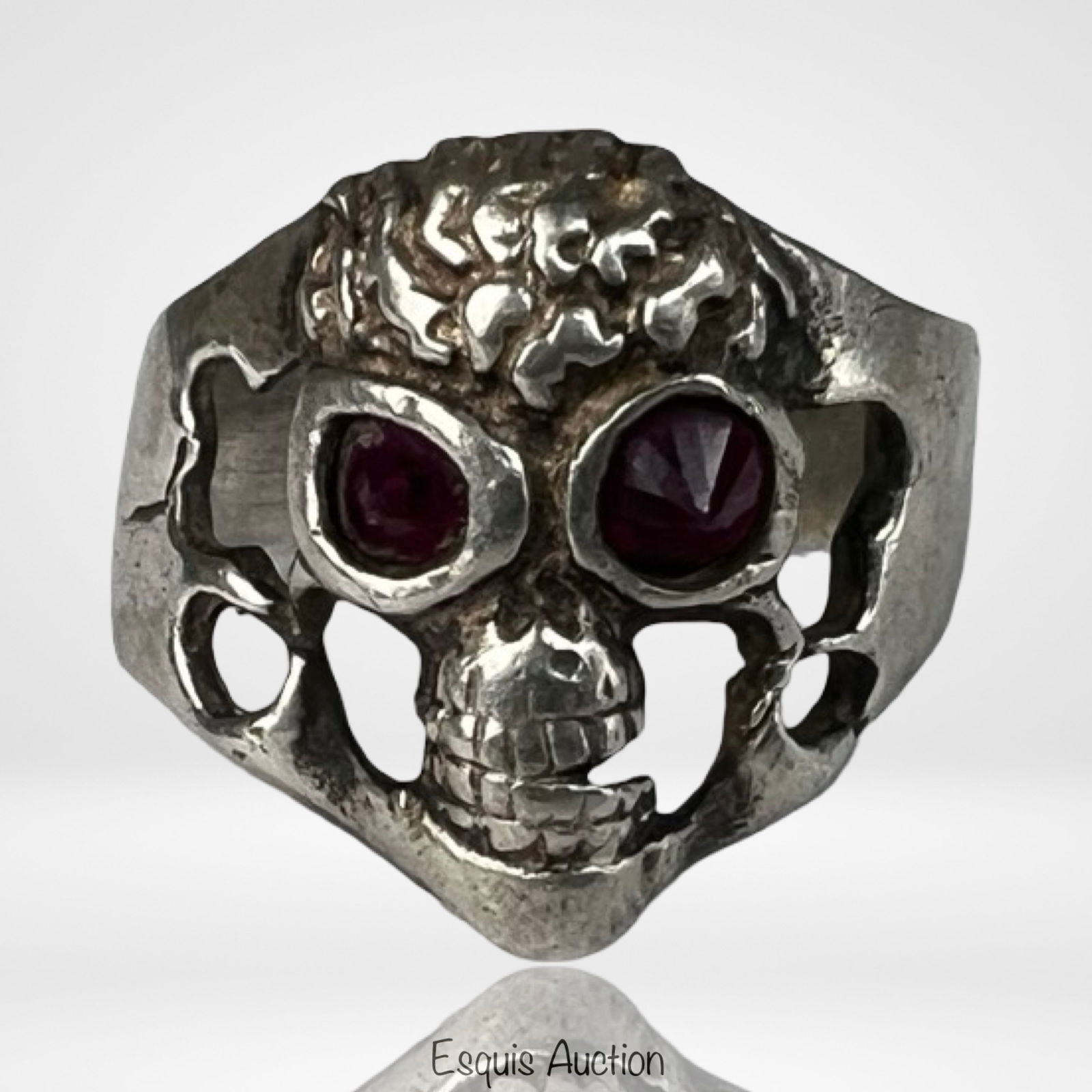 Sterling Silver Skull Ring with Red Eyes: Bold sterling silver skull ring featuring a detailed three-dimensional design with deep-set red stone eyes. The sculpted skull displays textured features, openwork sides, and a substantial band that g