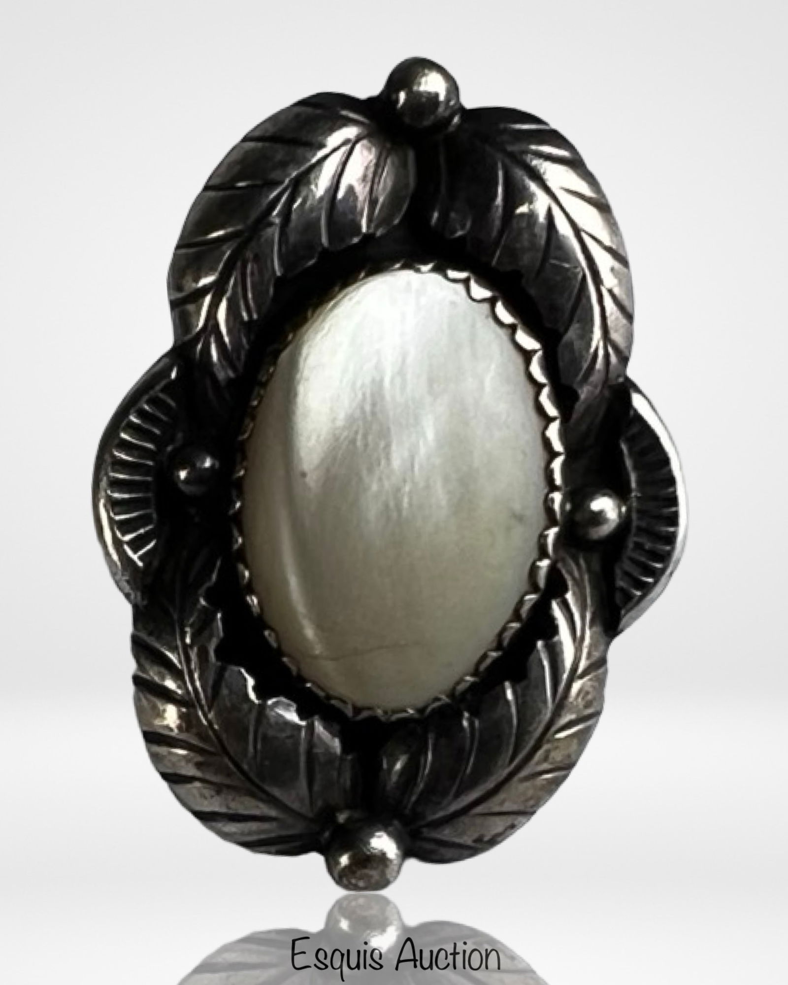 Native American Sterling & Mother of Pearl Ring: Striking sterling silver ring featuring an oval mother of pearl cabochon set within an intricately detailed leaf and bead motif. The luminous shell centerpiece is framed by hand-tooled silverwork, sho