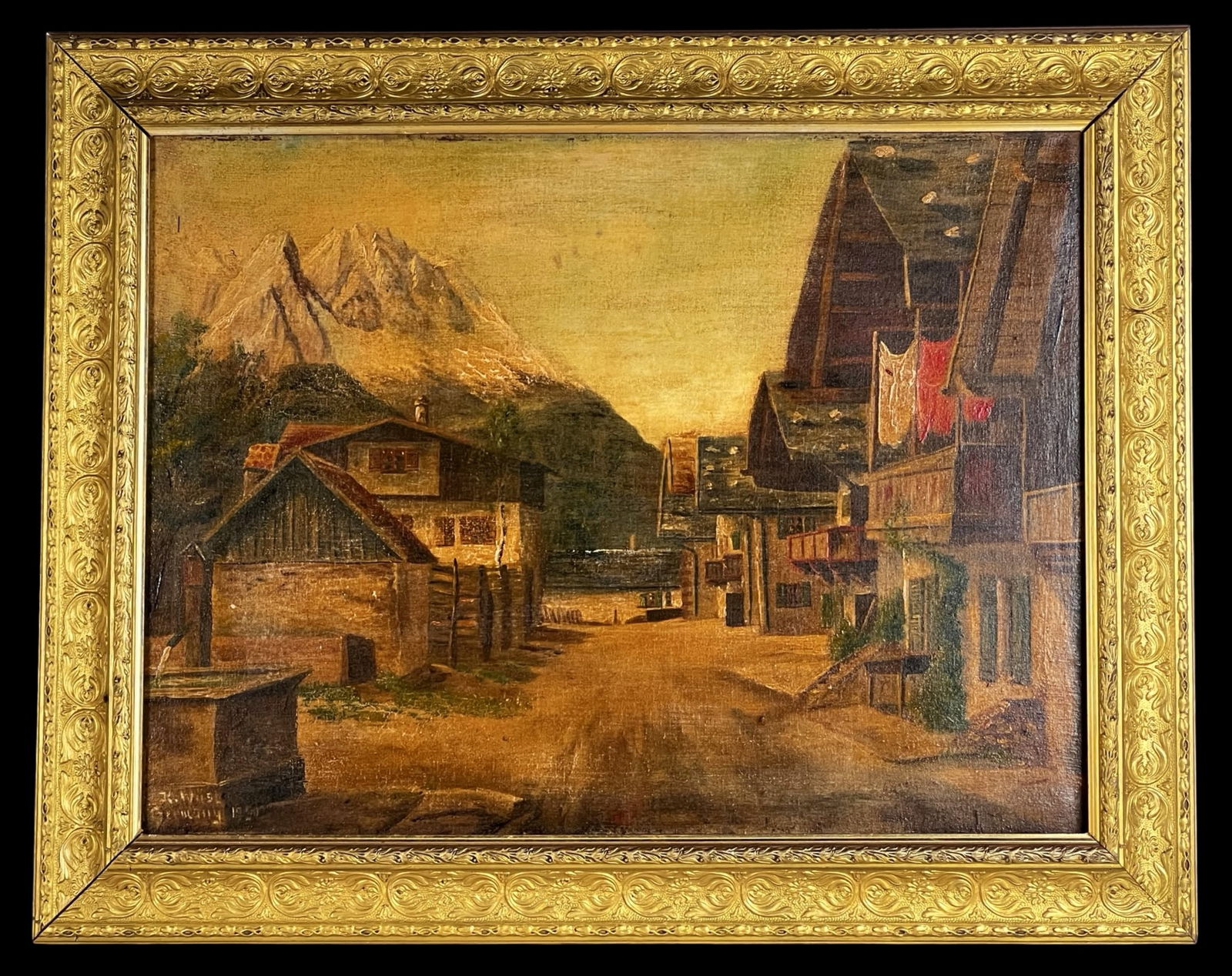 K. Wust German 1950 Alpine Village Oil Painting: Charming mid 20th century oil painting on canvas depicting a Bavarian alpine village with the dramatic peak of Zugspitze rising in the background. The composition features rustic timber buildings,