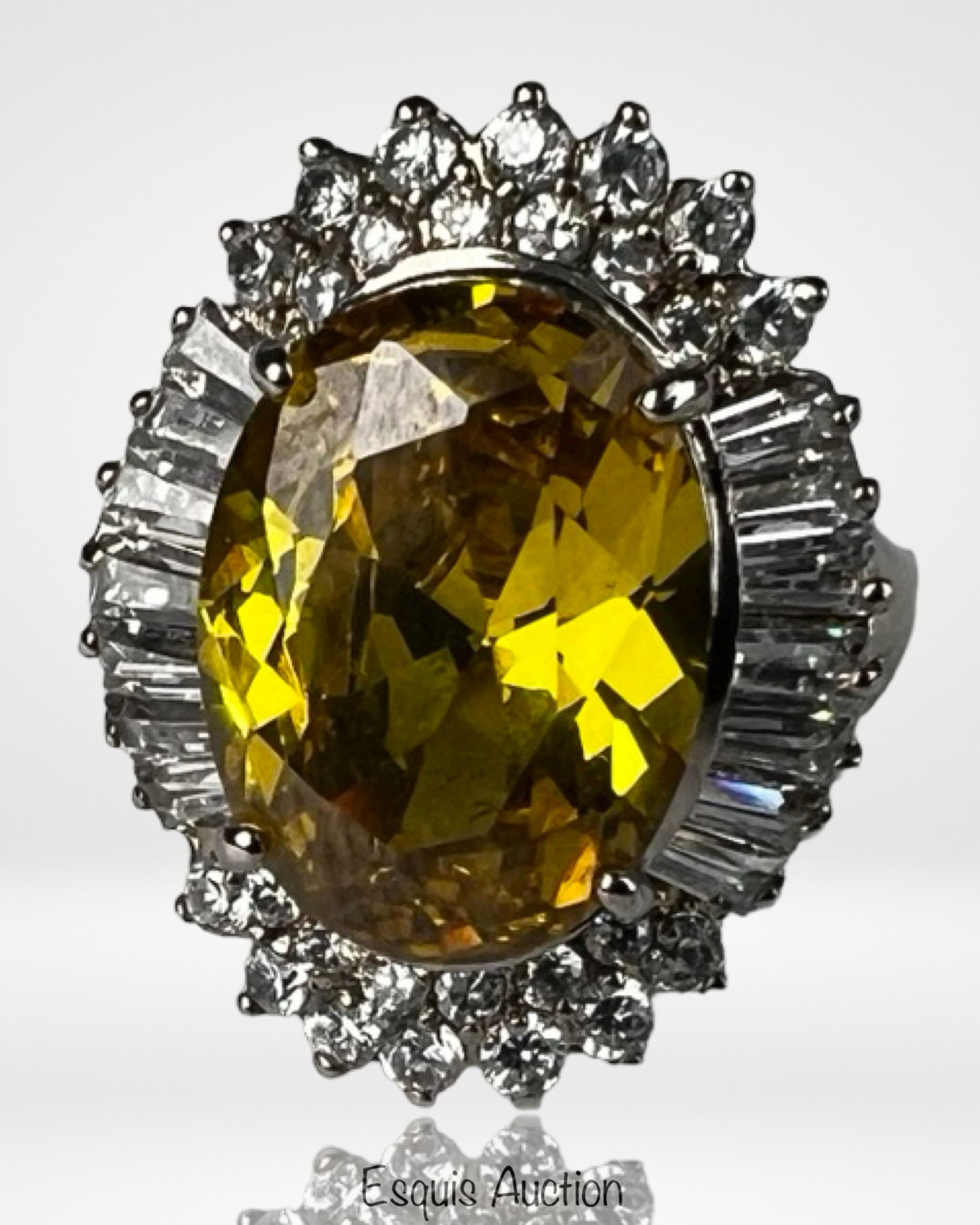 Sterling Silver Statement Cocktail Ring: Bold sterling silver cocktail ring featuring a large oval faceted yellow gemstone surrounded by a halo of sparkling round stones and flanked by tapered baguette-cut accents. The elevated openwork