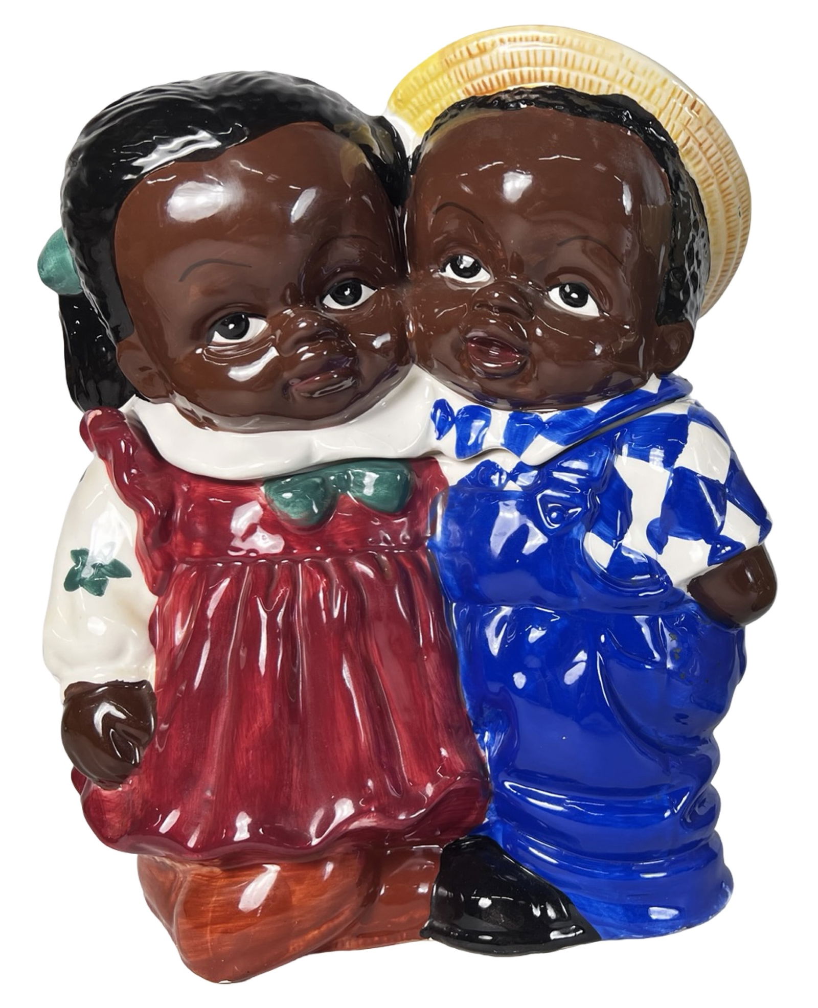 Children Hugging Cookie Jar: Charming figural ceramic cookie jar depicting two children affectionately hugging. The boy is dressed in blue overalls with a straw hat, while the girl wears a red dress with green hair bows. Their