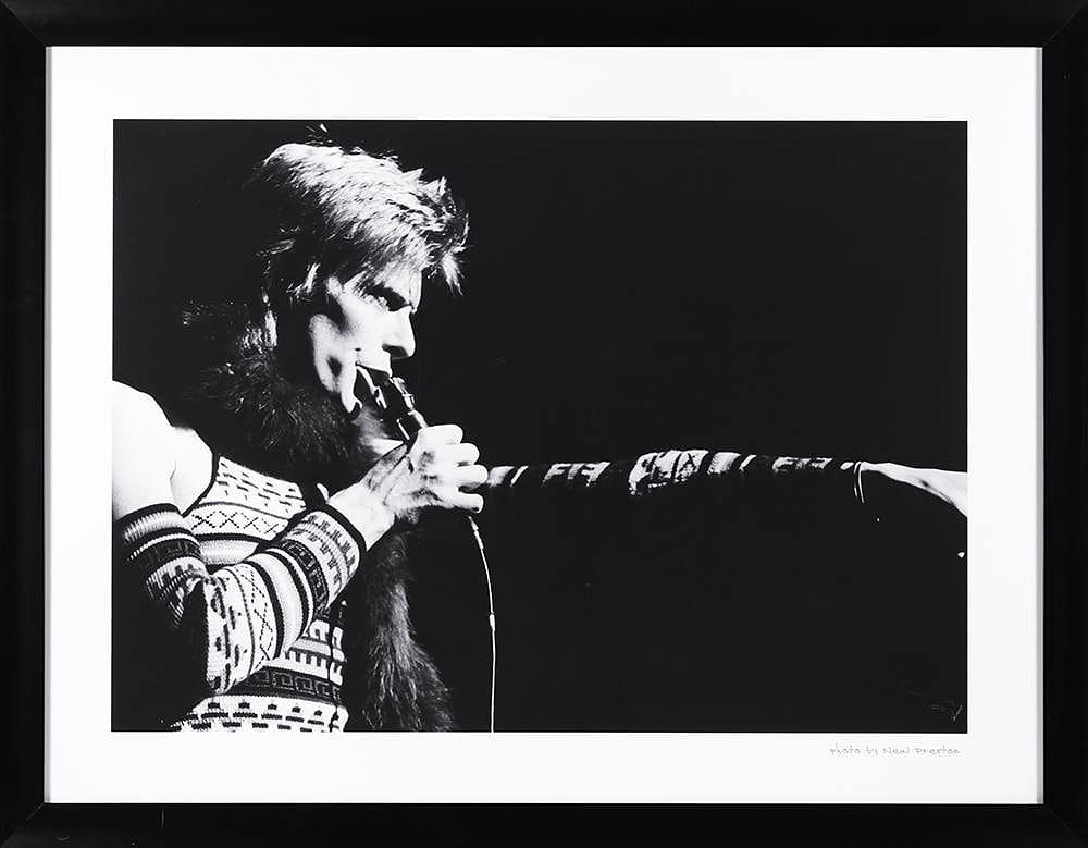 David Bowie Photo by Neal Preston Hard Rock Hotel: Striking black and white concert photograph of legendary rock musician David Bowie performing live on stage, captured by acclaimed rock photographer Neal Preston. The dramatic image shows Bowie in