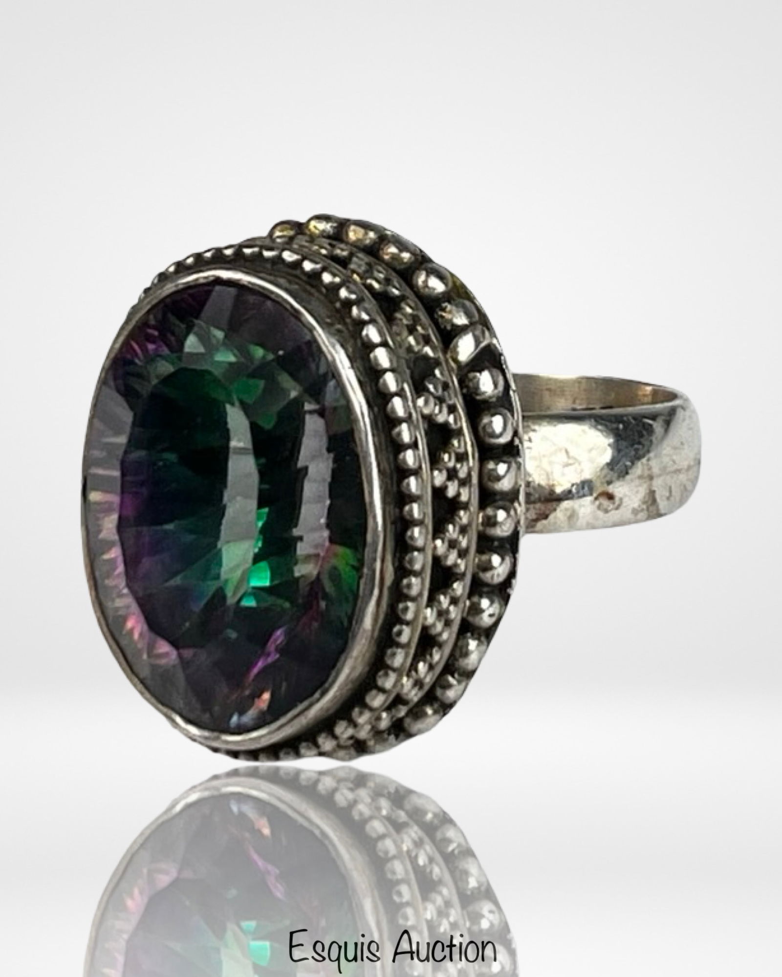Sterling Silver Mystic Topaz Statement Ring: Bold sterling silver statement ring featuring a large oval faceted mystic topaz, displaying vibrant iridescent hues of green, purple, and blue that shift beautifully with the light. The gemstone is