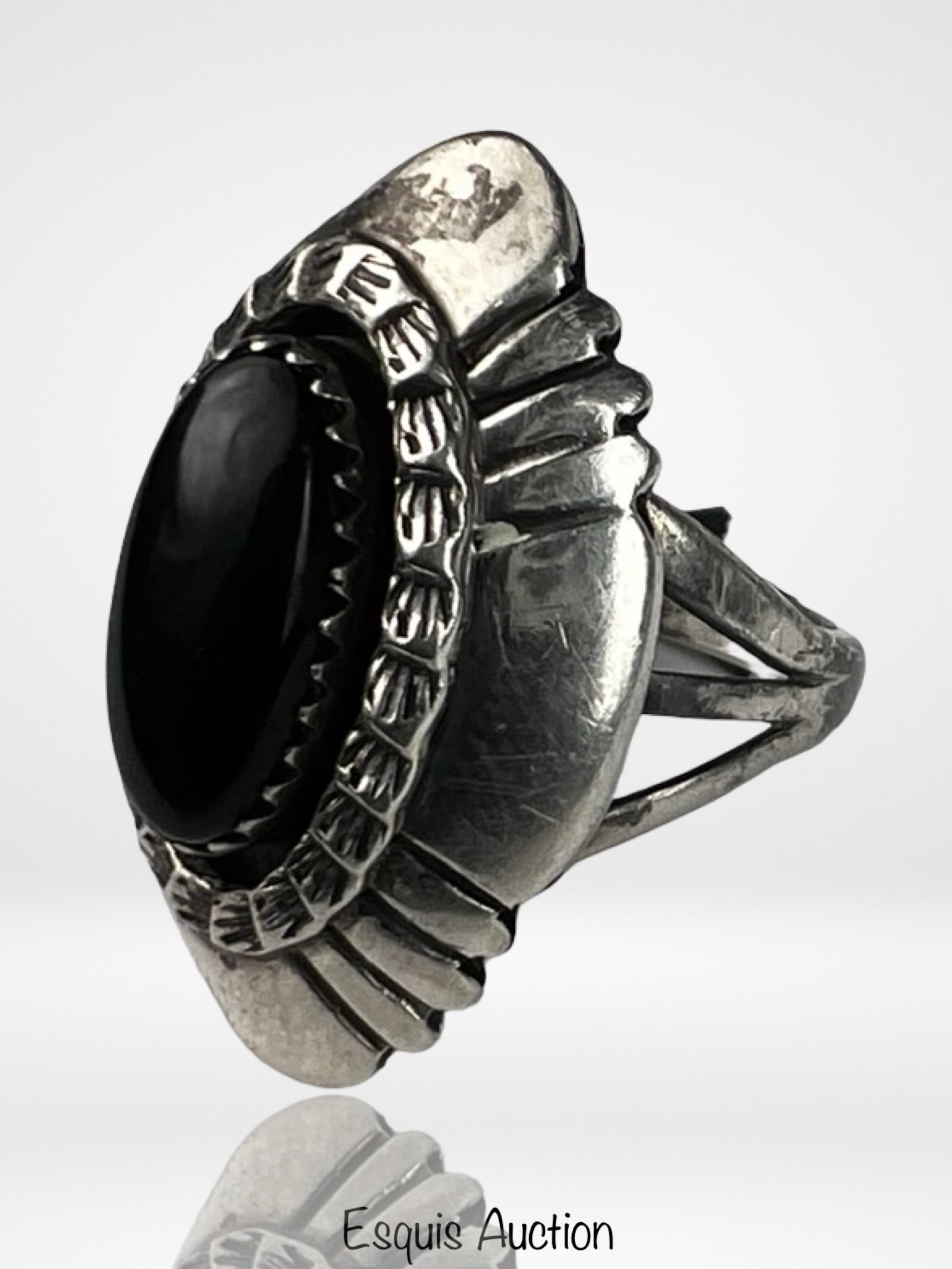 John Delvin Navajo Sterling Silver Black Onyx Ring: Striking Navajo sterling silver ring by John Delvin featuring a bold oval black onyx cabochon set within a serrated bezel. The substantial setting is framed by hand-stamped decorative elements, while
