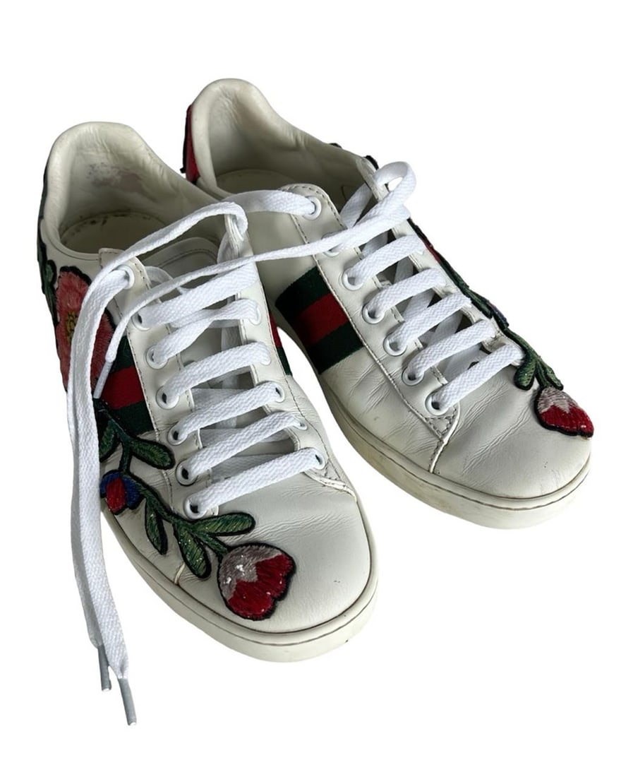 Gucci New Ace Floral Embroidered Leather Sneakers: These Gucci New Ace sneakers feature white leather uppers beautifully detailed with vibrant floral embroidery and classic green-red-green web stripes. Designed with metallic red and green snakeskin