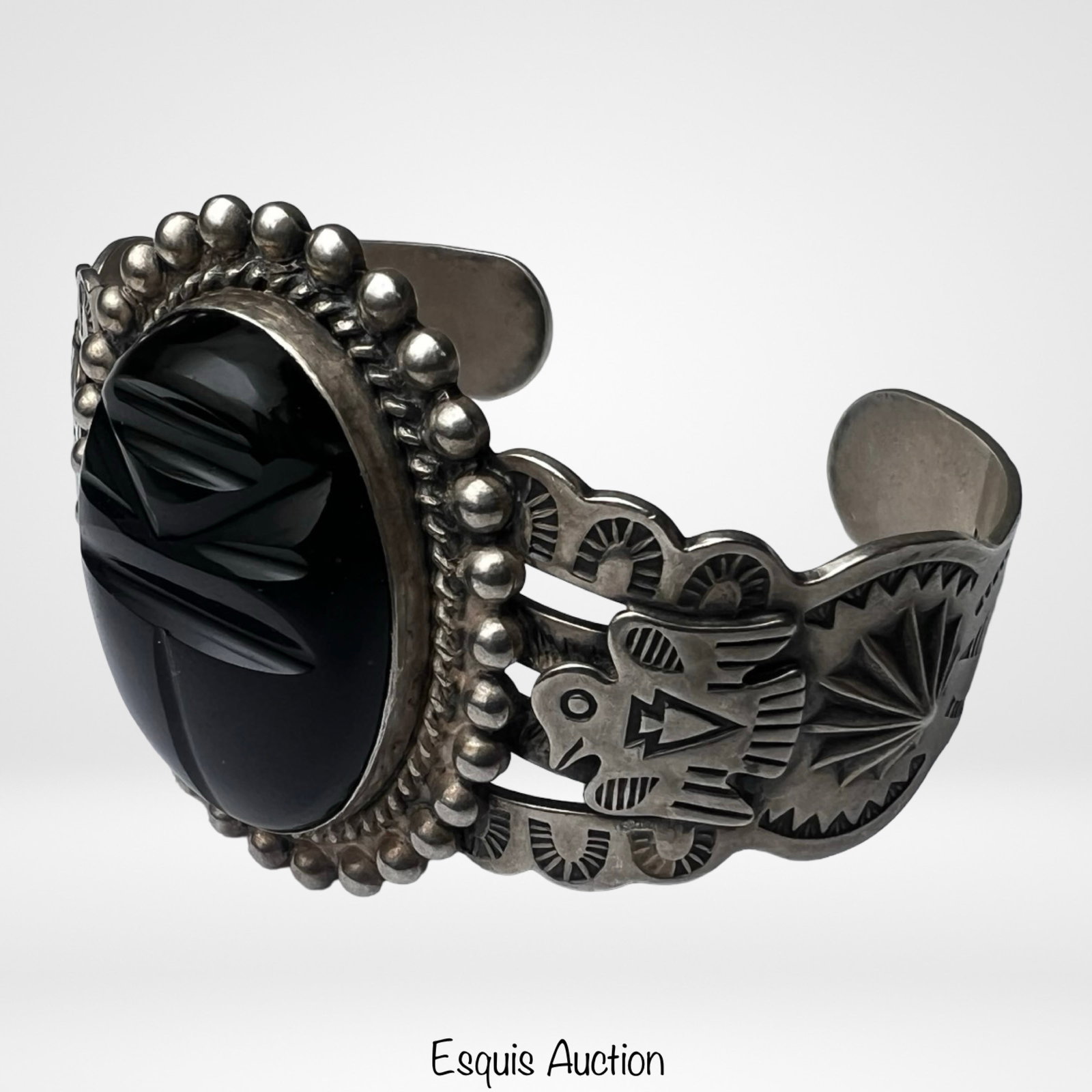 Navajo Sterling Silver Onyx Thunderbird Bracelet: Striking Native American Navajo sterling silver cuff bracelet featuring a large oval carved black onyx centerpiece. The cuff is richly decorated with traditional hand-stamped motifs, including