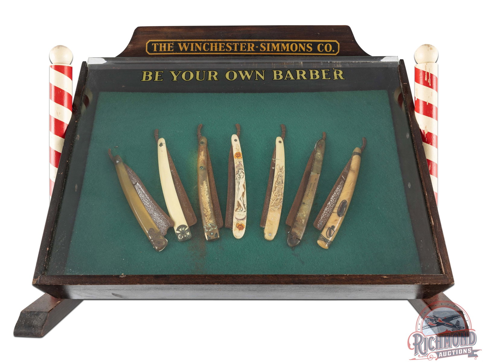 Winchester-Simmons Co. Be Your Own Barber Countertop Barber Tools Display Case w/ 7 Razors: Red mahogany-finished case, mounted with two miniature red and white striped ball-top barber poles, one on each side. Case sits at an angle with sliding glass front and green cloth liner. Case is very
