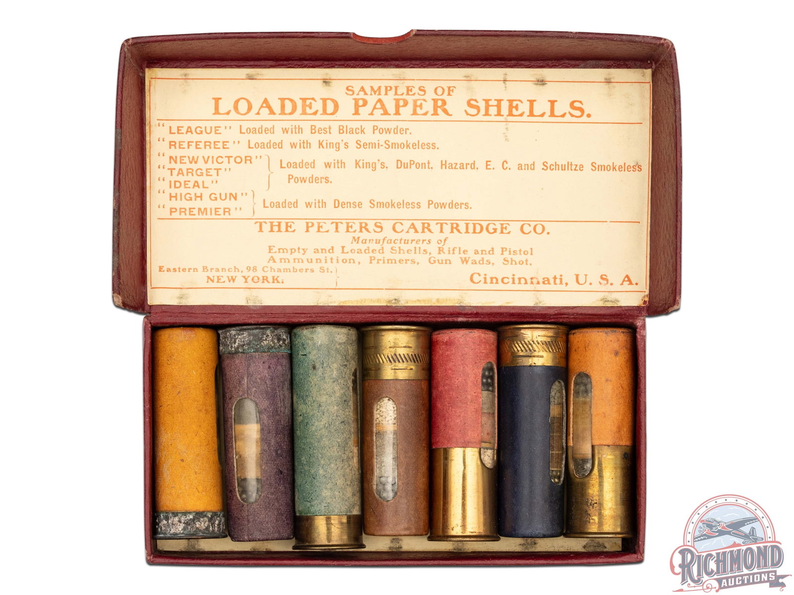 Peters Cartridge Company Salesman 12 GA Dummy Sample Kit: Peters Cartridge Company of Cincinnati, Ohio. 12 Gauge seven piece shotgun shell dummy kit with label listing "LEAGUE, REFEREE, NEW VICTOR, TARGET, IDEAL, HIGH GUN, & PREMIER". Kit is in a hinged red 