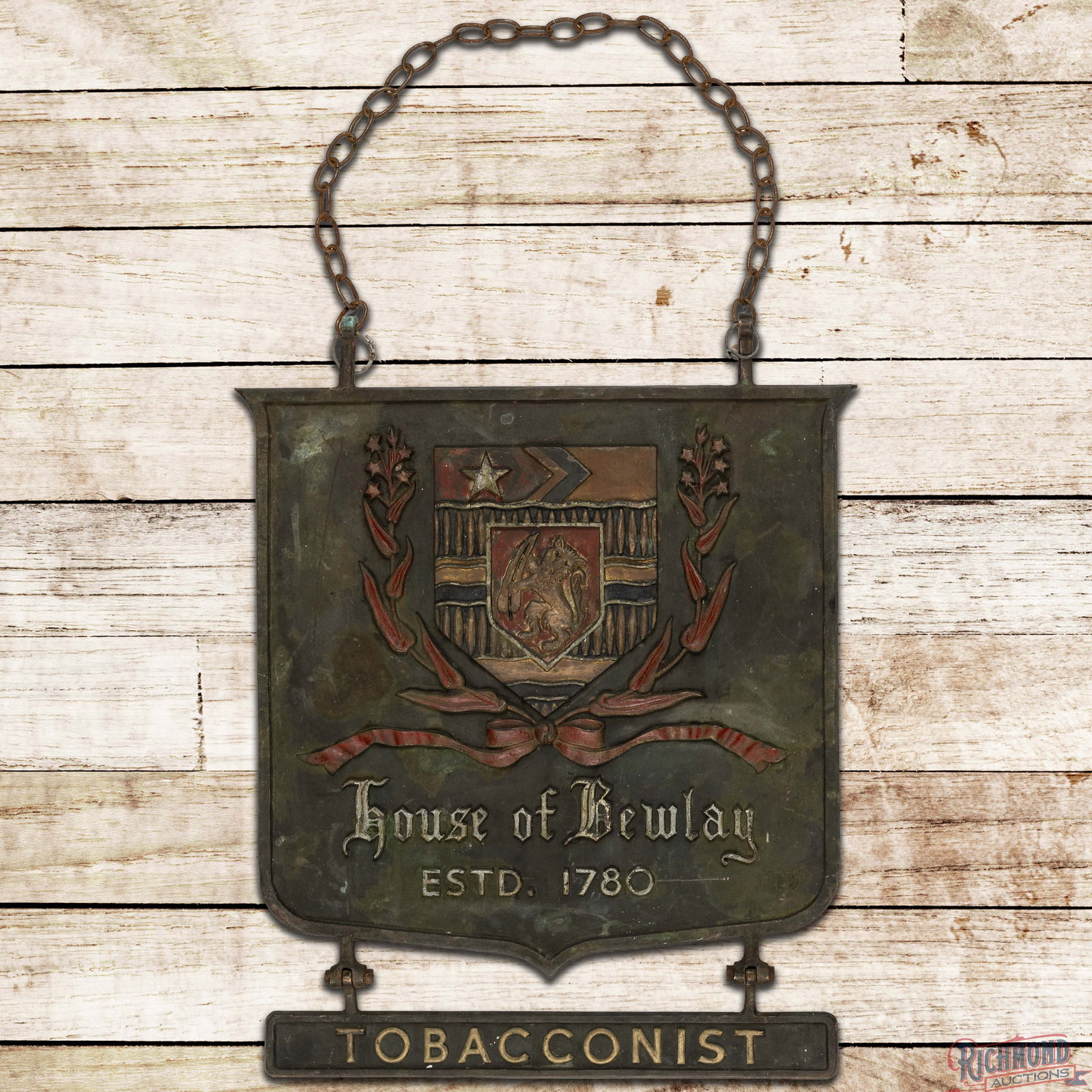 House of Bewlay Est. 1780 Tobacconist DS Cast Iron Shield Sign w/ Crest: Double sided heavy cast iron embossed shield with "Tobacconist" attachment has good color. The display retains factory paint with areas of surface wear throughout. The reverse has additional paint