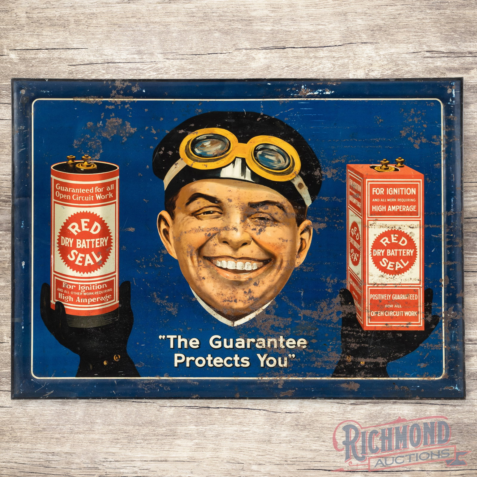 Red Seal Dry Battery "The Guarantee Protects You" Single Sided Tin Sign: SST (single sided tin) self-framed sign with a cardboard reverse has good color and shine. The display has striking graphics with areas of wear and paint loss. The perimeter has light bends with simil