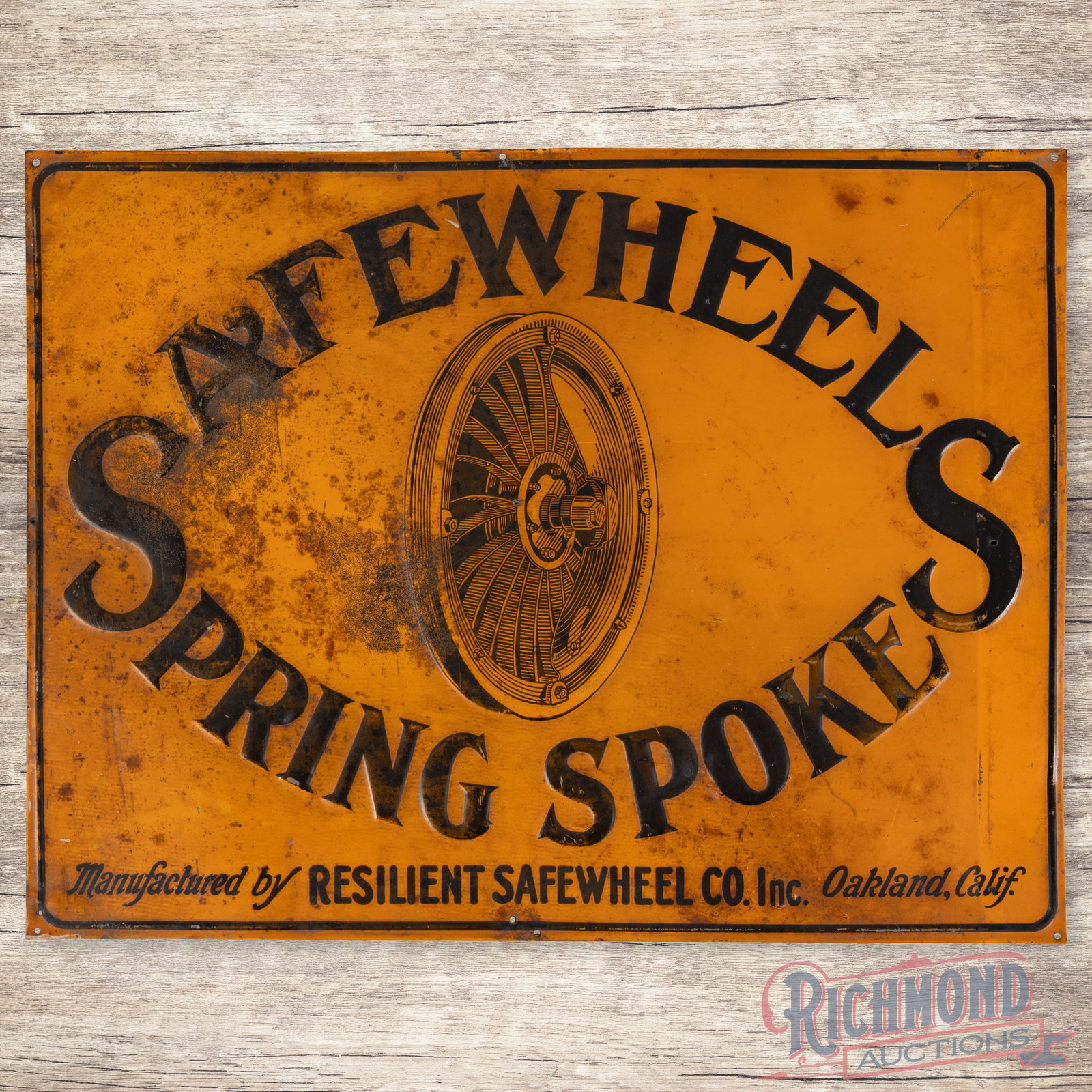 Safewheel Spring Spoke Emb. Single Sided Tin Sign Oakland California: SST (single sided tin) embossed self-framed sign has good color and moderate shine. The display has wear with oxidation and discoloration. The "S" in the right field has a small non-factory hole and t