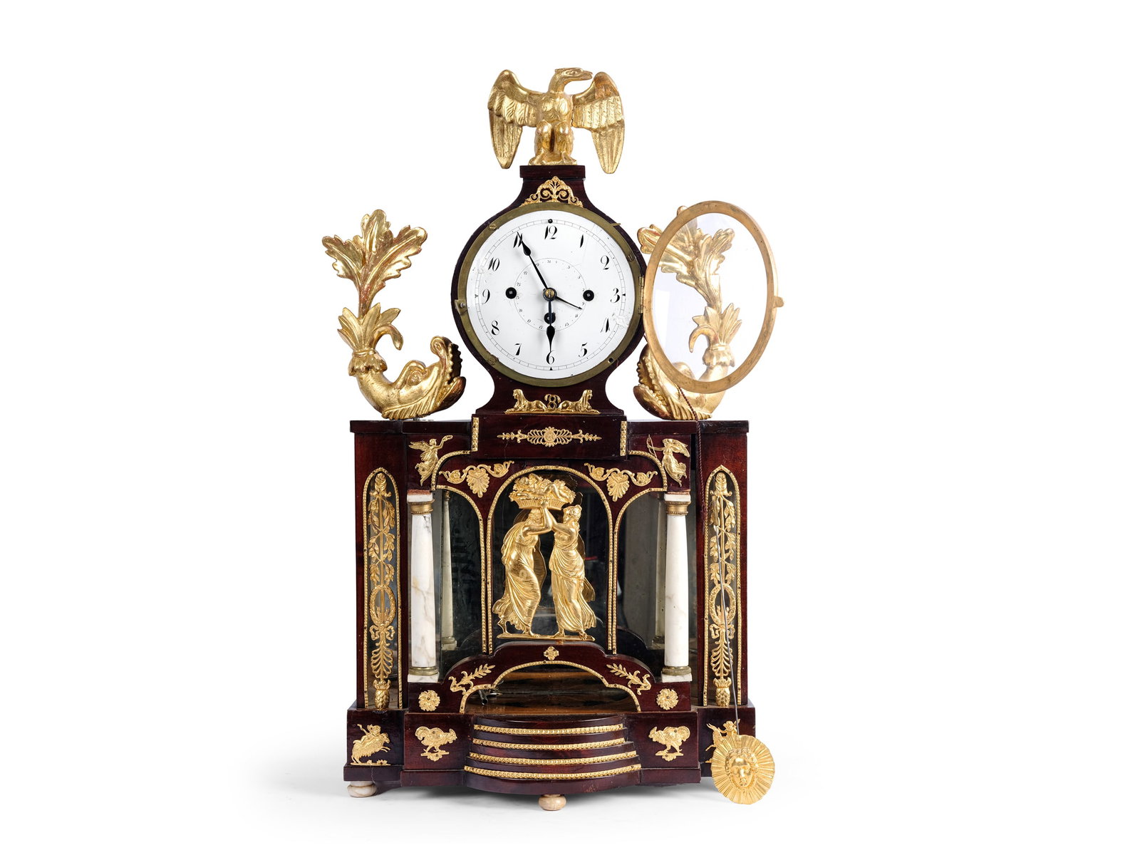 EMPIRE CHEST CLOCK, MAHOGANY CASE WITH GILDED BRASS APPLIQUES: Empire chest clockMahogany case with gilded brass appliquesDolphins and eaglesCarved and gilded wood, alabaster columnsViennese 4/4 hour strike with date displayHeight 63 cm, width 36 cmMovement not