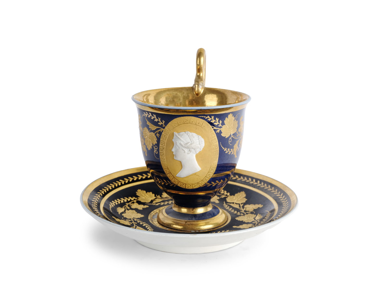 CUP WITH SAUCER, PORTRAIT MEDALLION IN BISQUE PORCELAIN AT CENTER: Cup with saucerPortrait medallion in bisque porcelain at centerSaucer marked "T" at centerEmpire period, circa 1800/20Blue-decorated and gilded porcelainHeight 12 cm, saucer diameter 14 cmMarked on
