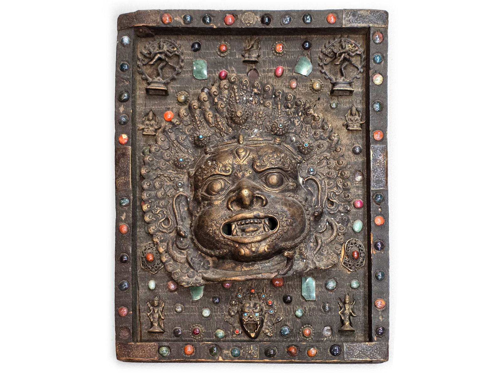 ANTIQUE RELIEF PANEL, TIBET, VARIOUS DEITIES IN BRONZE AS WELL AS DECORATIVE ORNAMENTS: Antique relief panel, TibetVarious deities in bronze as well as decorative ornaments, mostly in the form of semi-precious stones Mounted on a heavy wooden panel55 x 41 cm