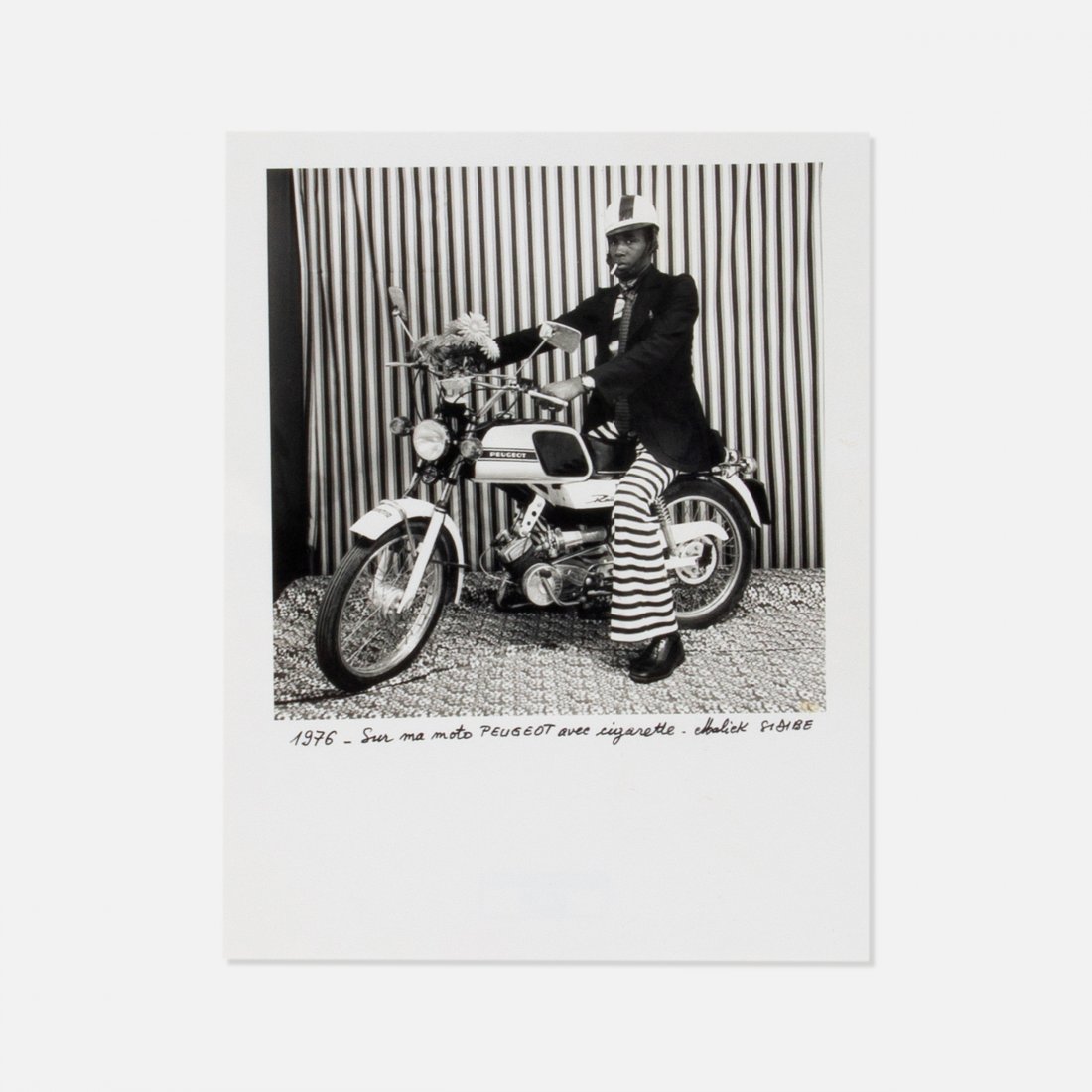 Malick Sidibe, Self Portrait: 1976 silver print 9.5" x 7 3/8" Photograph by Malick Sibide with writing translated to: "On my Peugeot motorcycle with cigarette" and signed. "Studio Malick" rubber stamp on verso. Provenance: Private